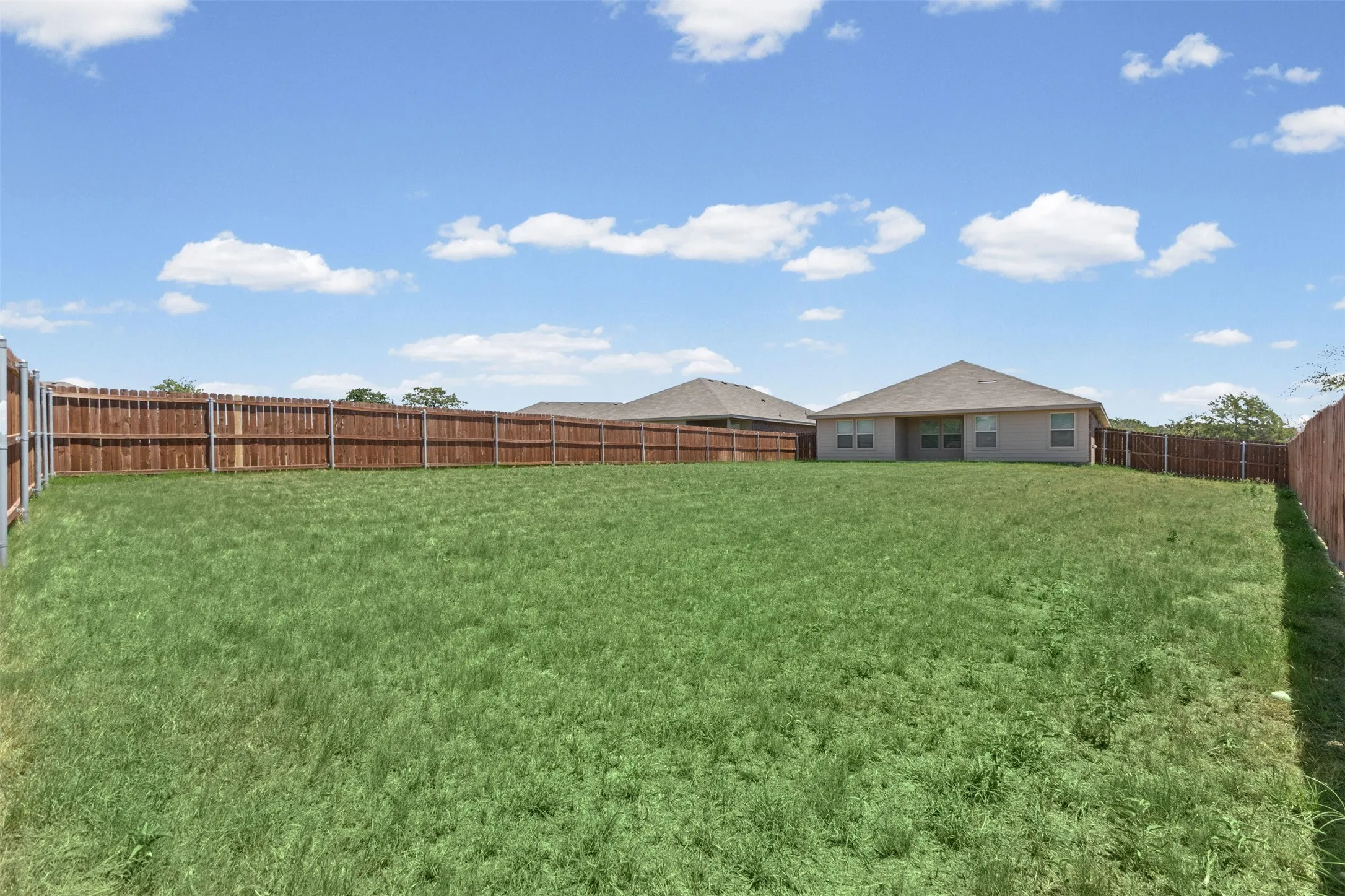 Expansive grass lawn bordered by a tall privacy fence, featuring a single-story residence in the background