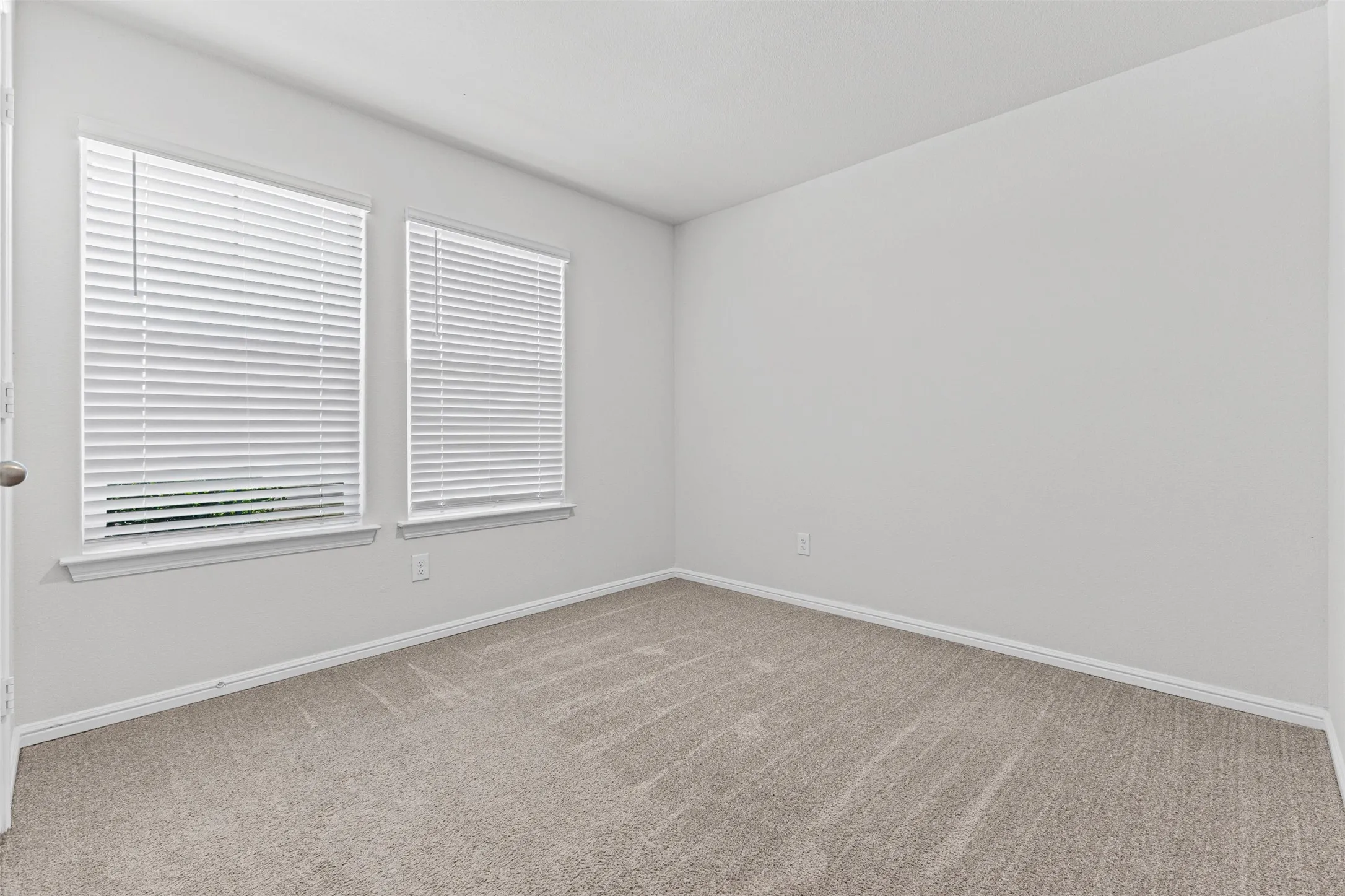 Carpeted room featuring two windows with white blinds, neutral wall paint, and white trim