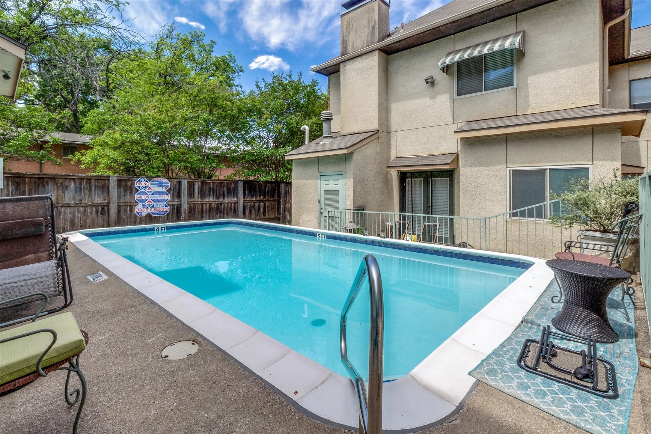 Rectangular swimming pool featuring a ladder, concrete decking, and a wood privacy fence