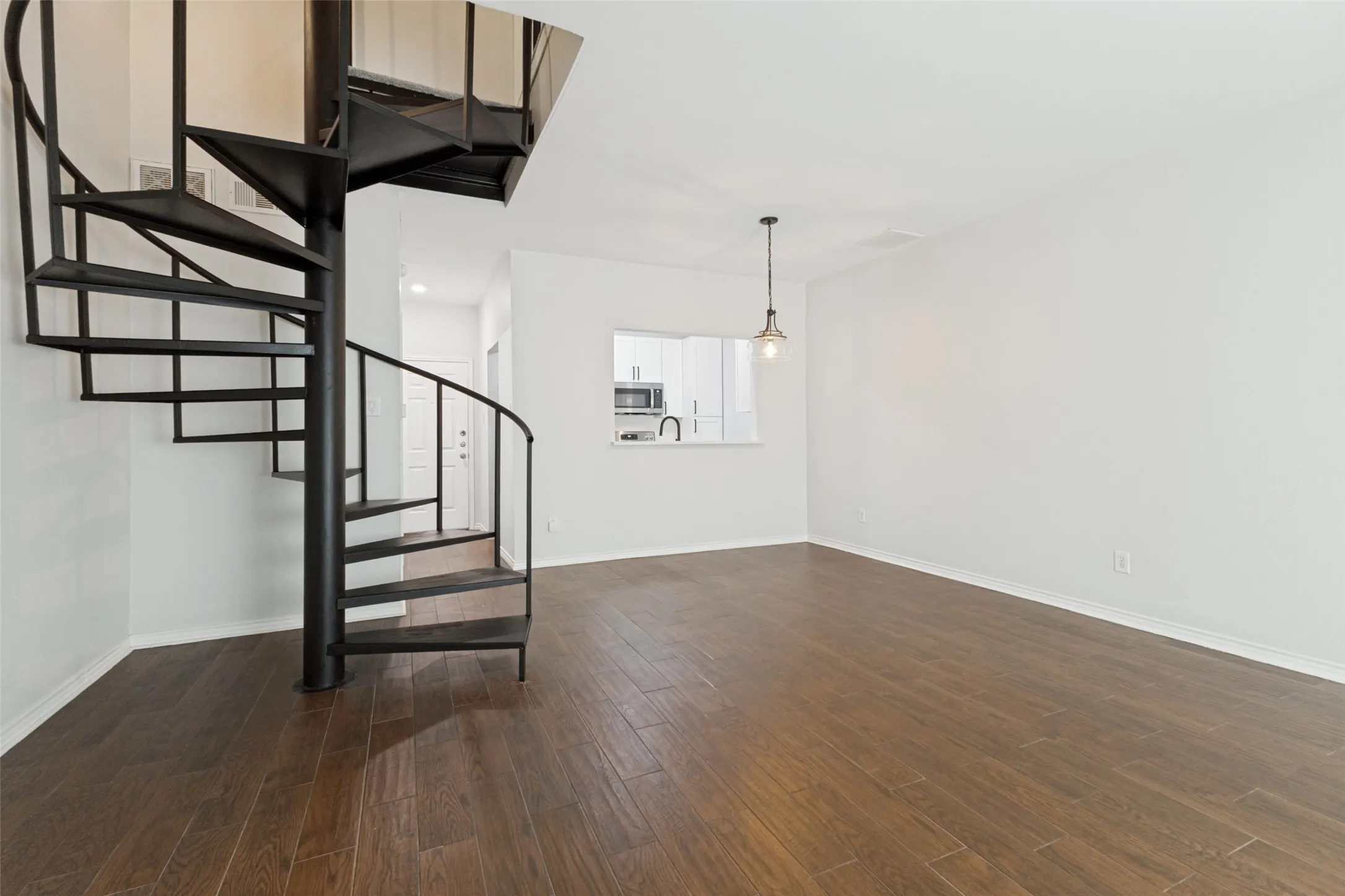 Spacious living area with dining area defined by light fixture featuring a prominent black spiral staircase and wood-finish flooring