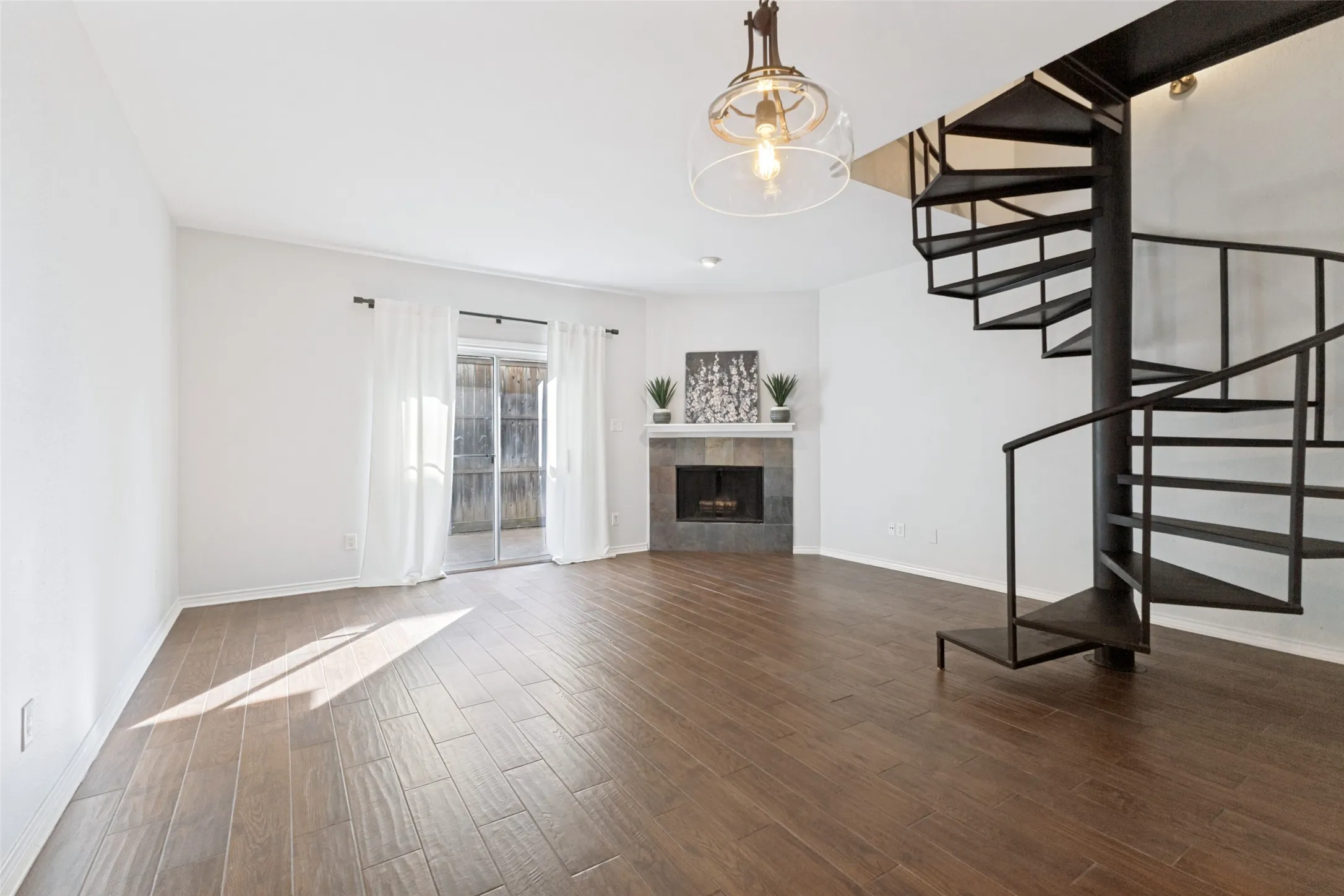 Open-concept living space featuring a black spiral staircase, wood-finish flooring, and a stone-faced corner fireplace with a white mantel