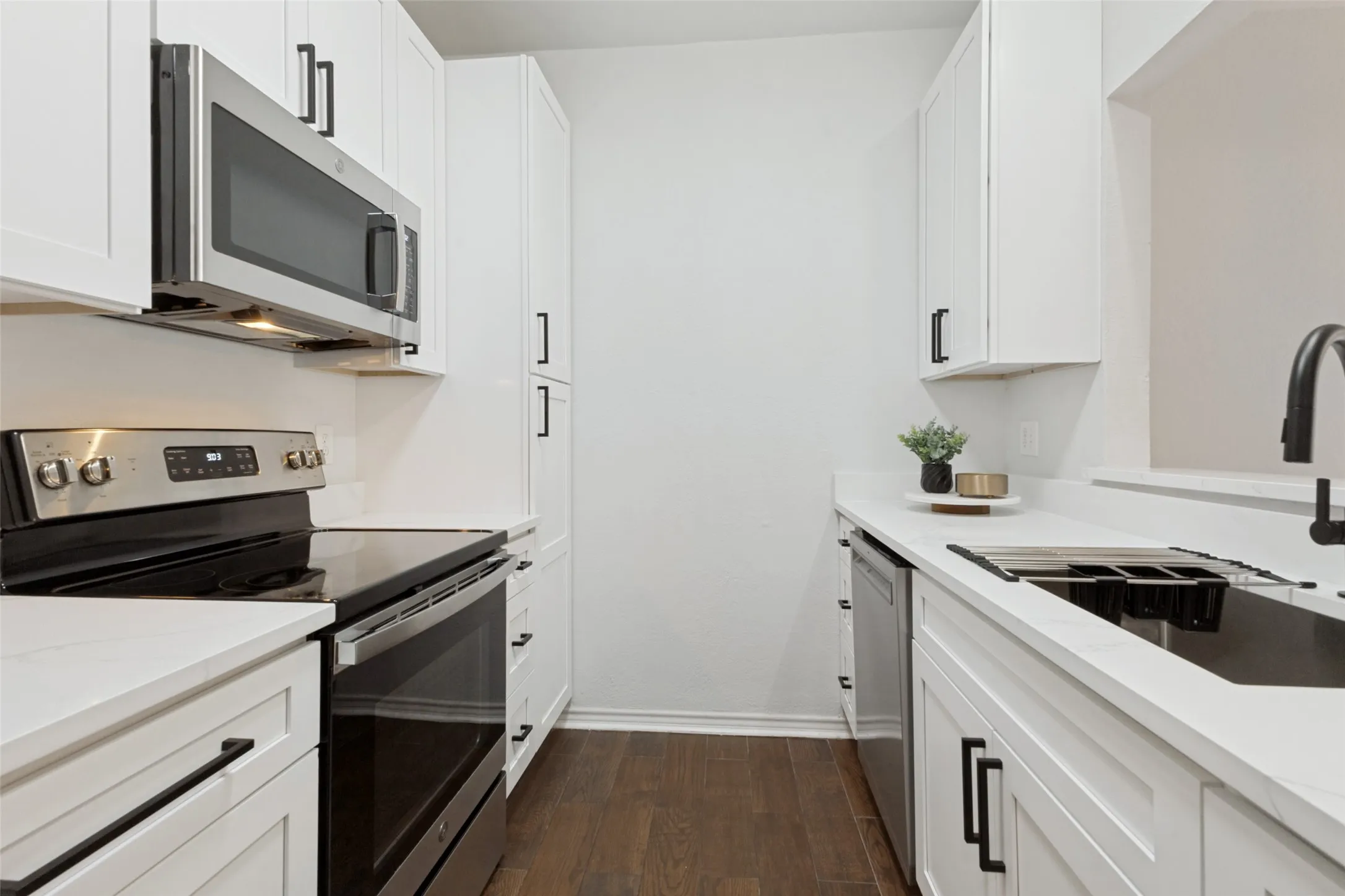 Fully renovated kitchen featuring white shaker cabinetry with matte black hardware, stainless steel appliances, quartz countertops, and wood-look flooring