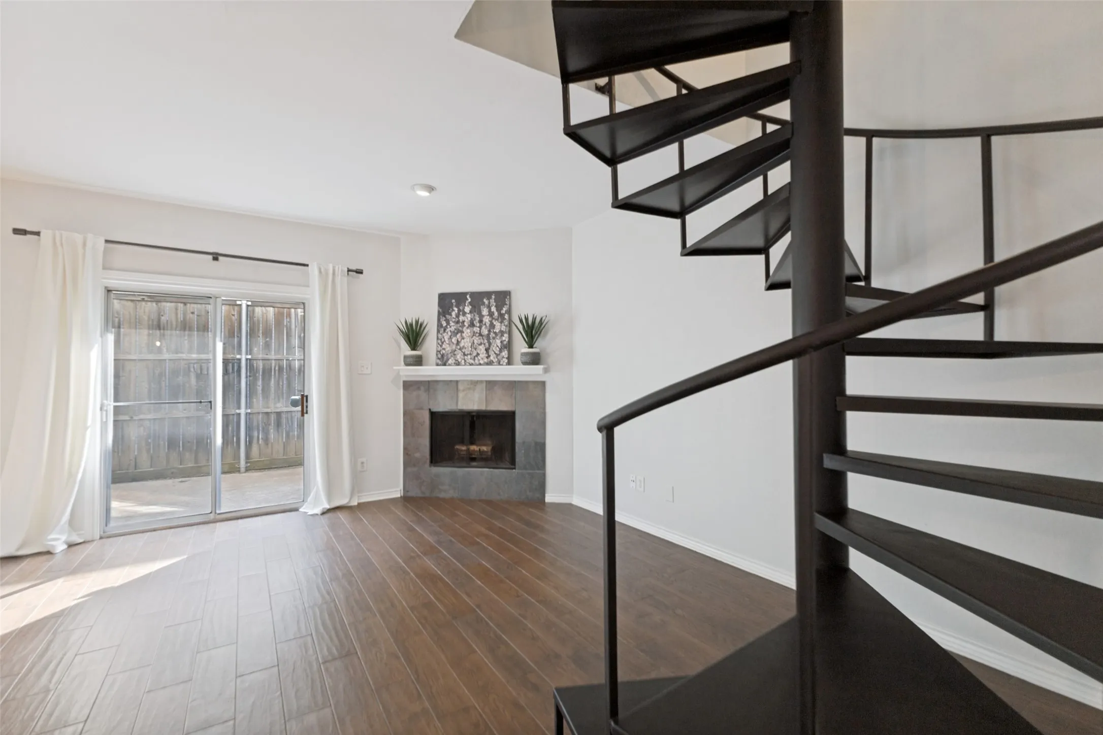 Open-concept living space featuring a black spiral staircase, wood-finish flooring, and a stone-faced corner fireplace with a white mantel