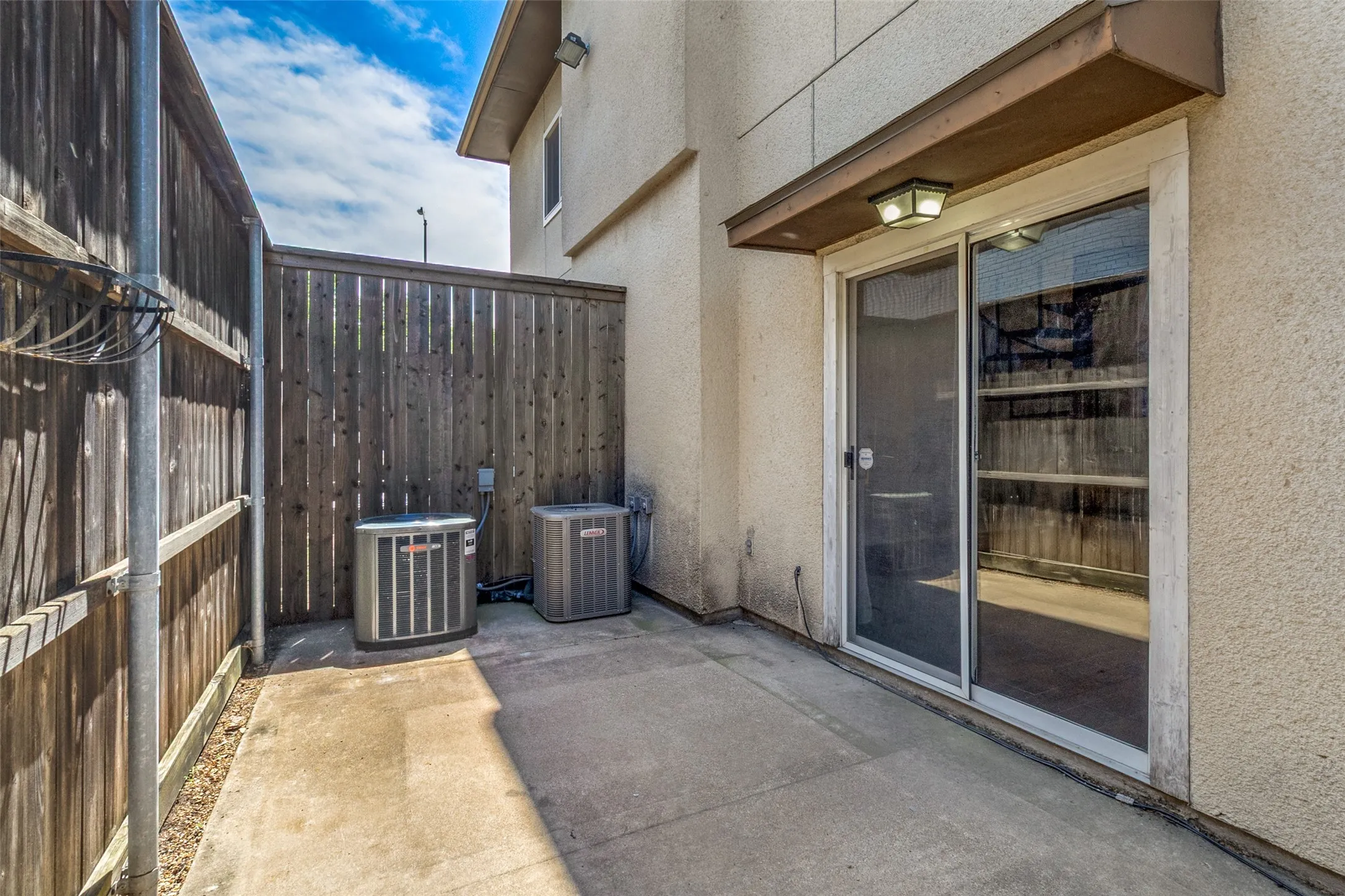 Private outdoor patio space featuring concrete flooring, a sliding glass door, and an exterior light fixture