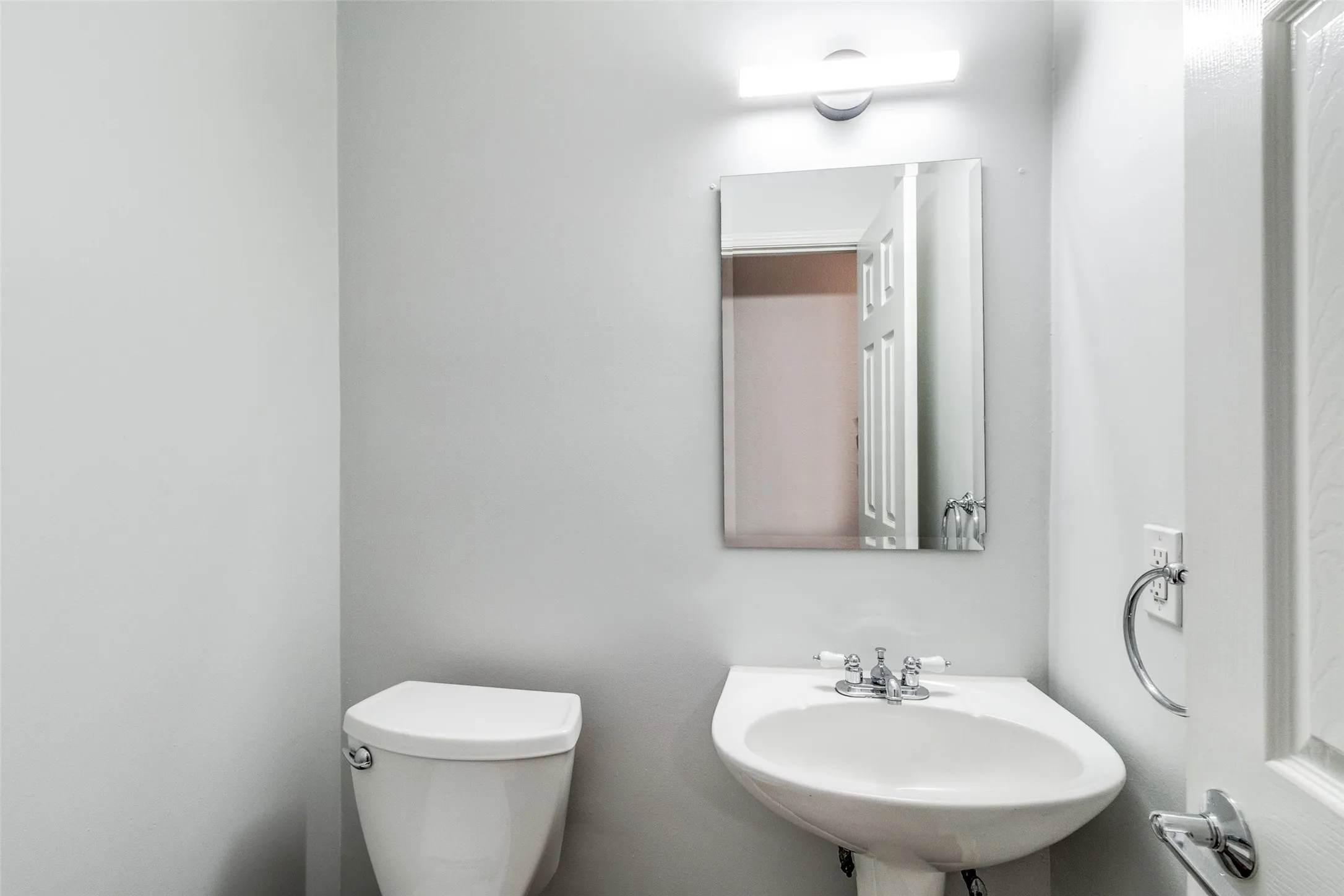 Pedestal sink with chrome faucet, rectangular mirror, and an overhead vanity light fixture
