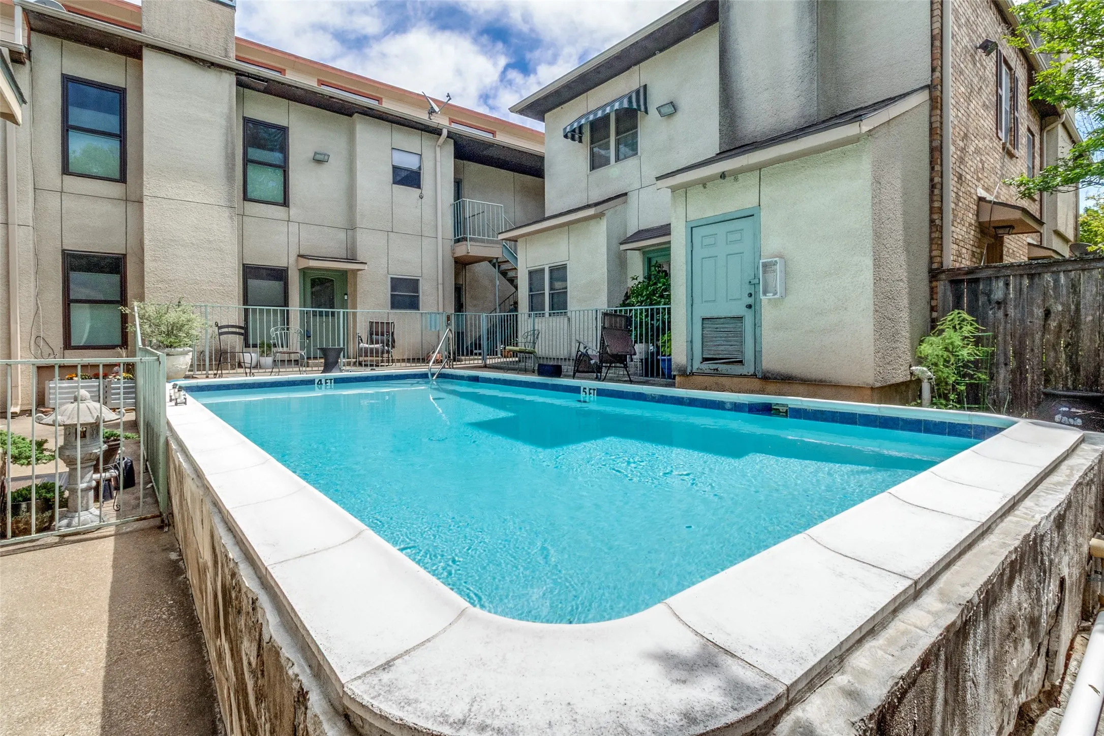 Outdoor swimming pool with concrete coping, stone-clad retaining wall, and metal railing