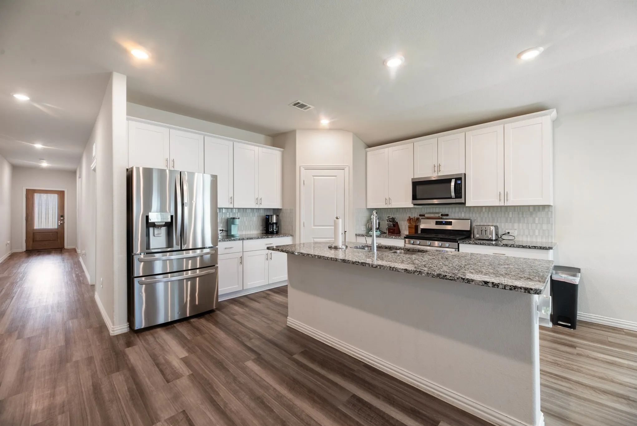 Modern kitchen featuring white cabinetry, stainless steel appliances, a center island with a sink, and granite countertops