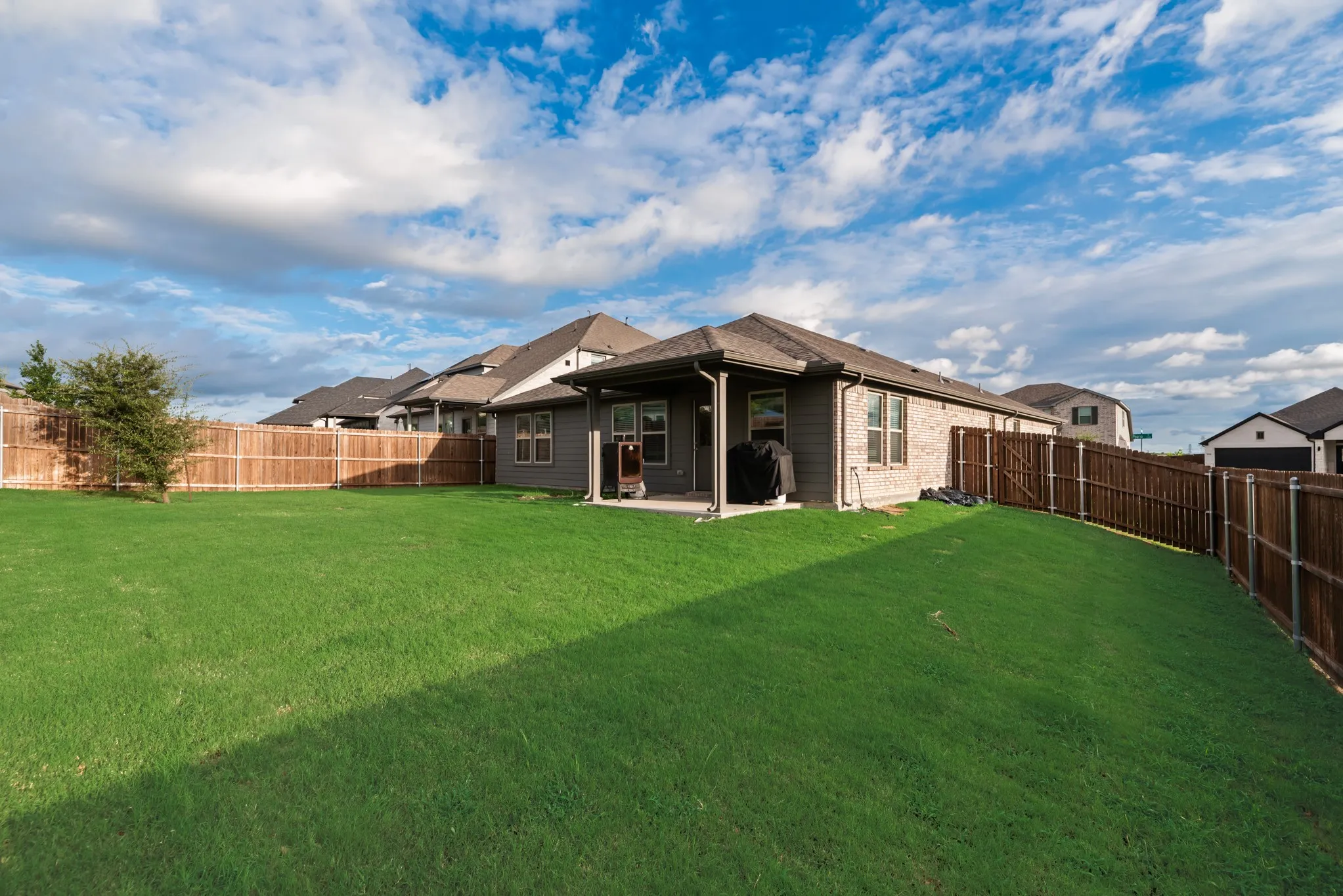 Expansive fenced backyard featuring a large green lawn and a covered patio