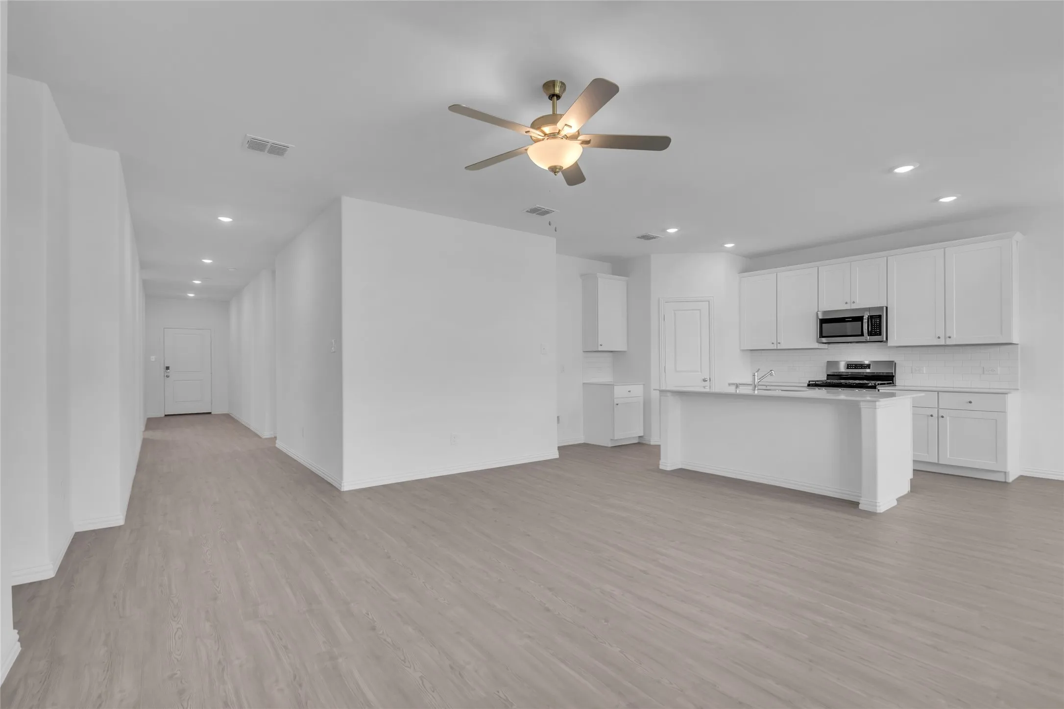 Kitchen featuring an island with sink, white cabinetry, light hardwood / wood-style flooring, stainless steel appliances, and ceiling fan