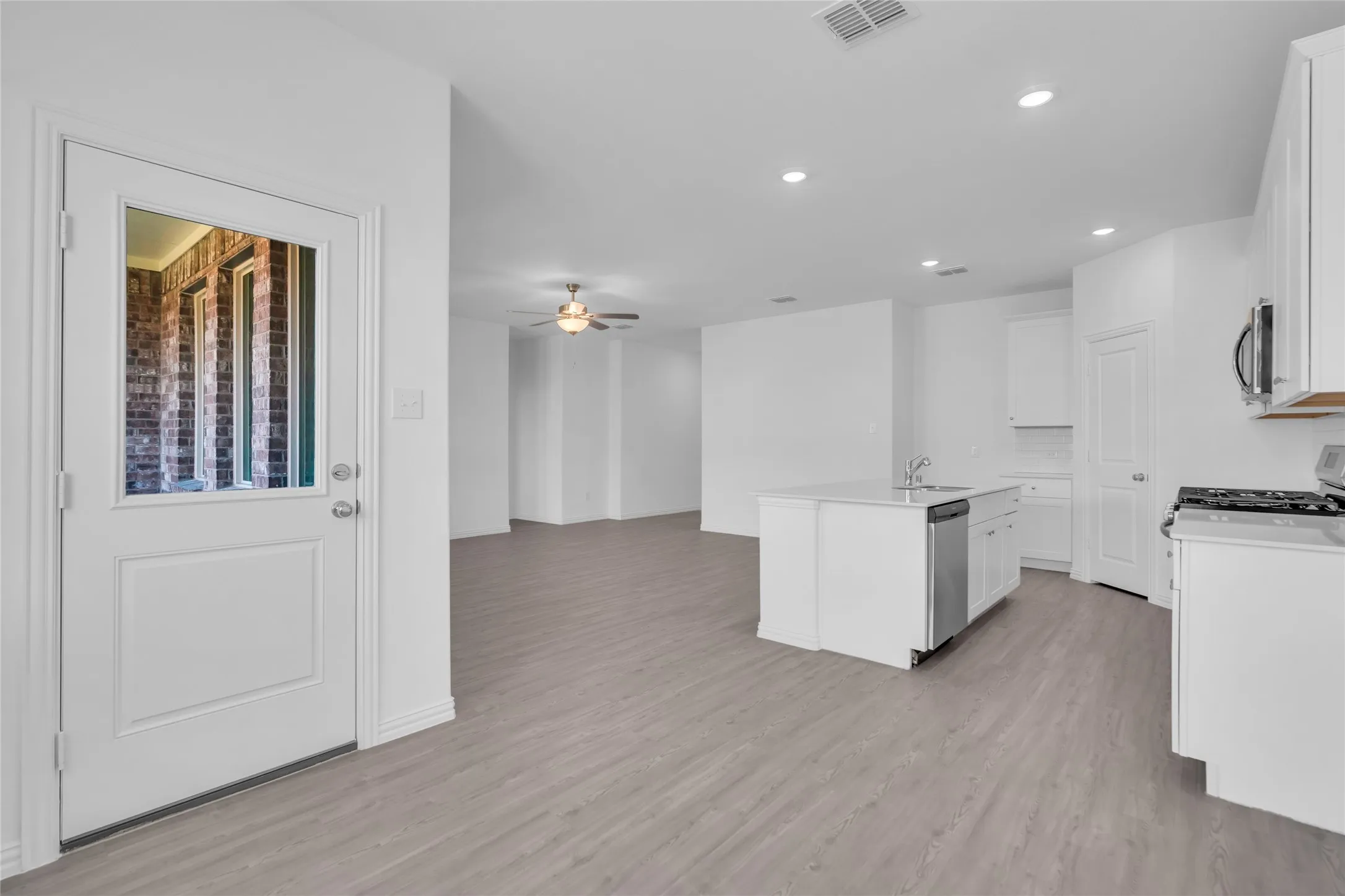 Kitchen featuring white cabinets, light hardwood / wood-style flooring, a center island with sink, appliances with stainless steel finishes, and ceiling fan