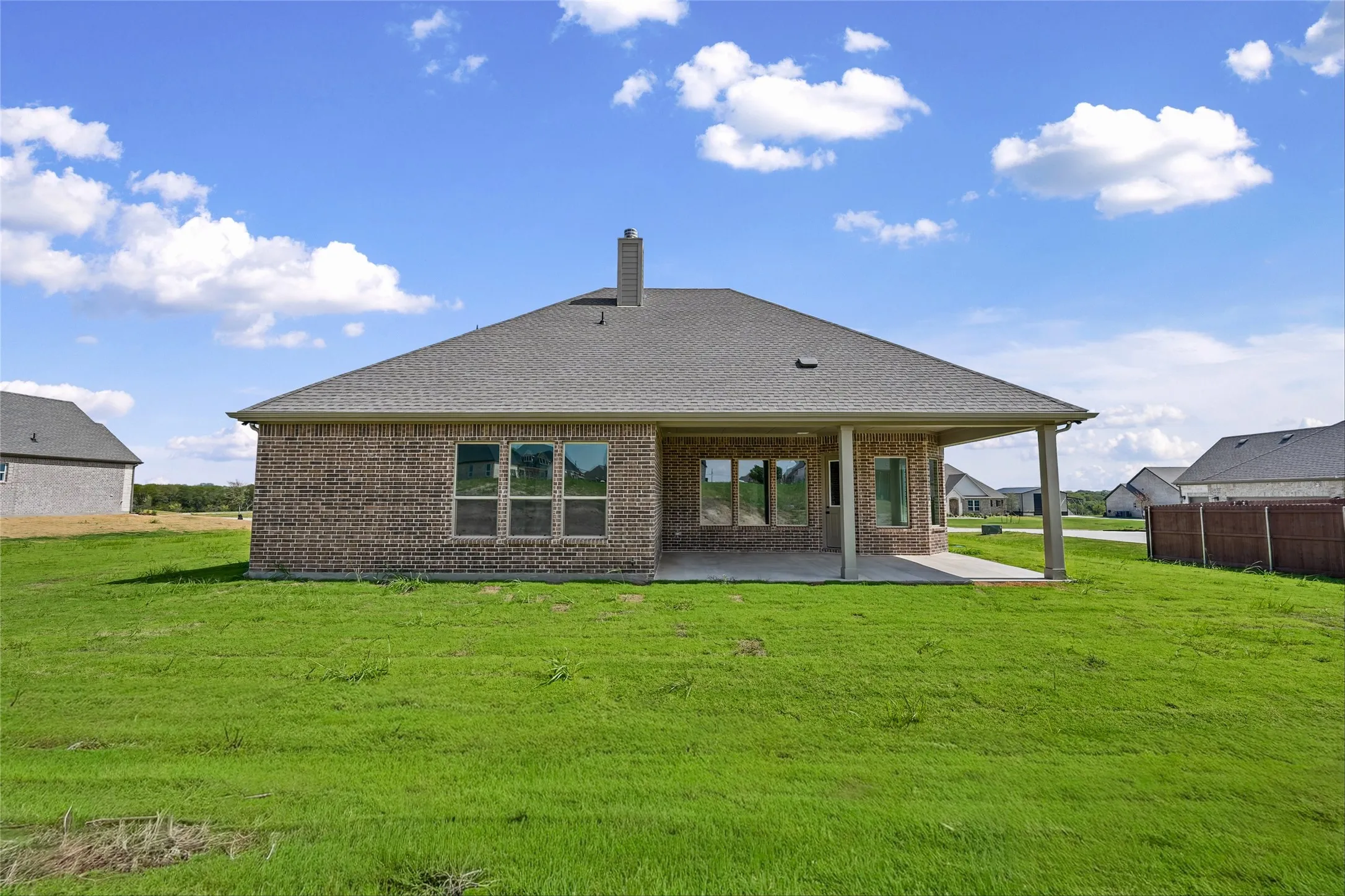 Brick exterior, covered patio, large windows, attached chimney, and a composite shingle roof
