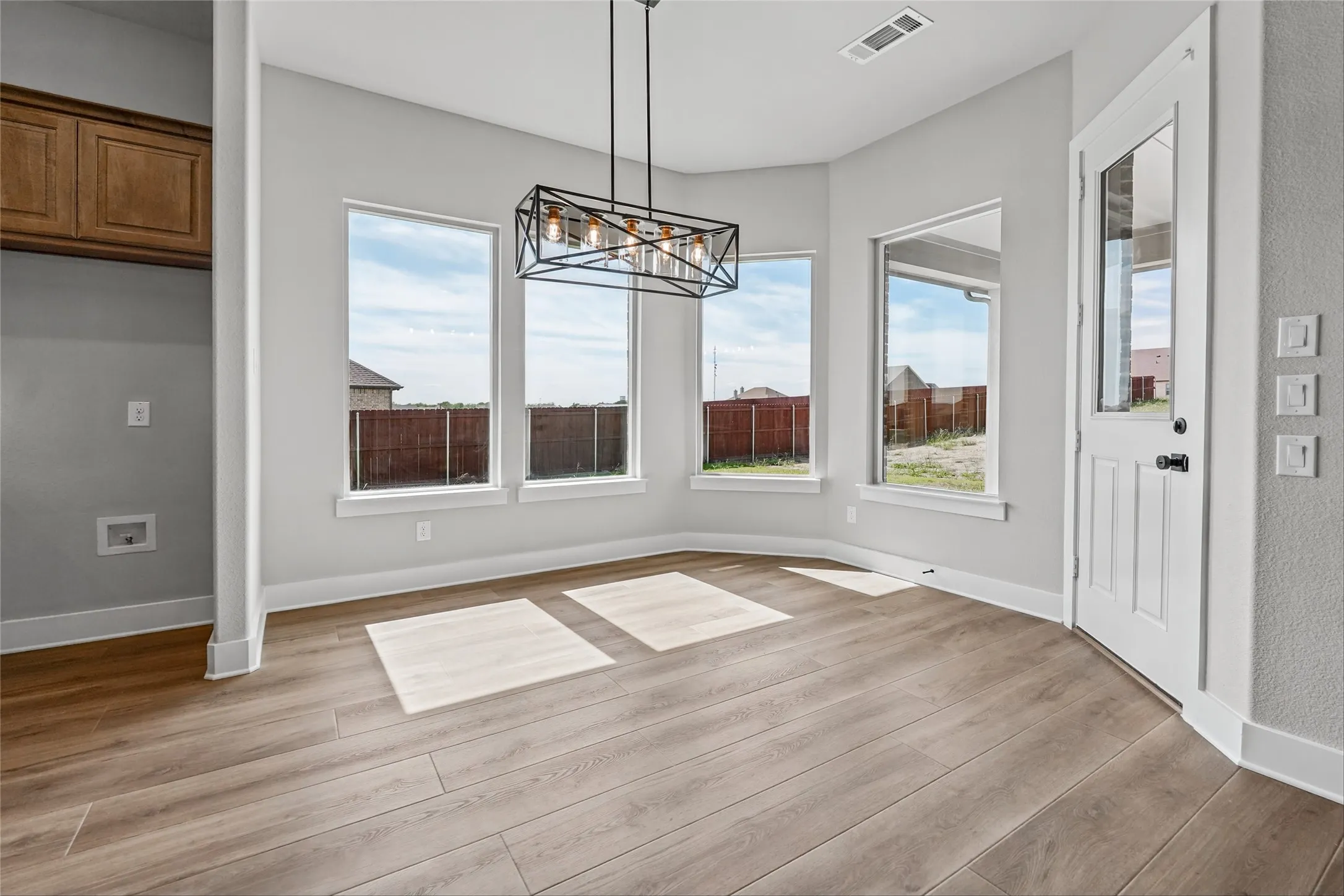 Spacious dining area featuring wood-finish flooring, a contemporary linear chandelier, multiple windows, and a glass-paneled door