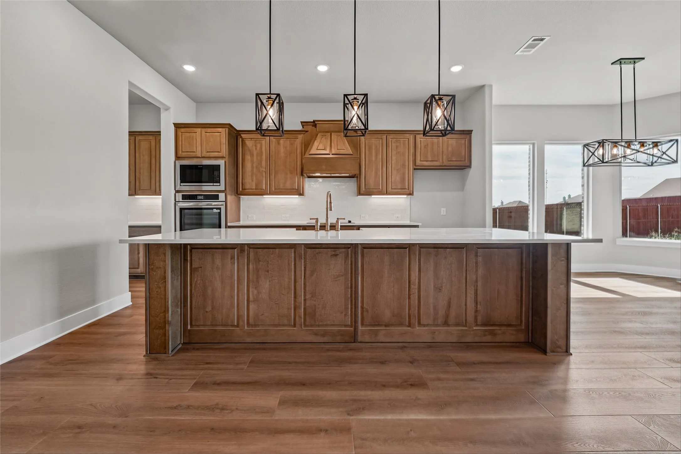 Kitchen island with panel detailing, integrated stainless steel appliances, wood-finish flooring, and pendant lighting