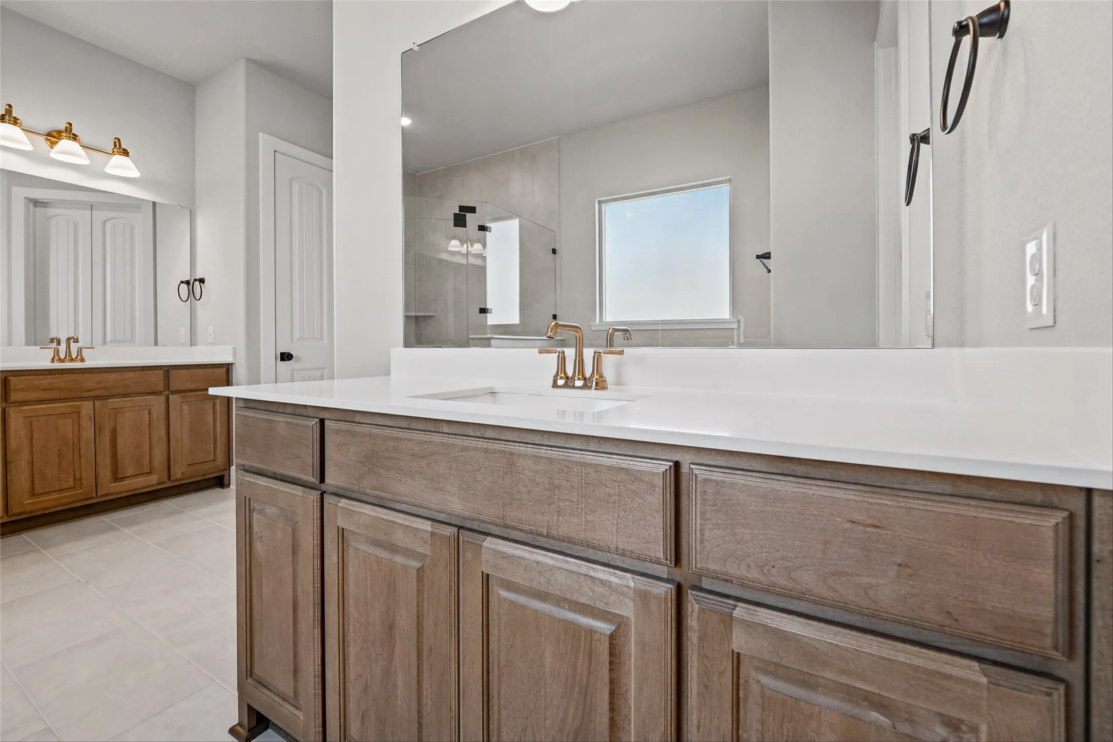 Dual vanities with white countertops, wood-finish cabinetry, and gold-tone fixtures