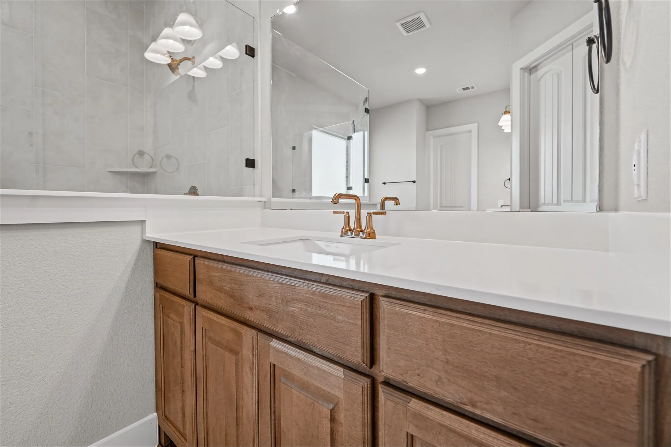 Wood-finish vanity with white countertop, undermount sink, and brass-finish faucet