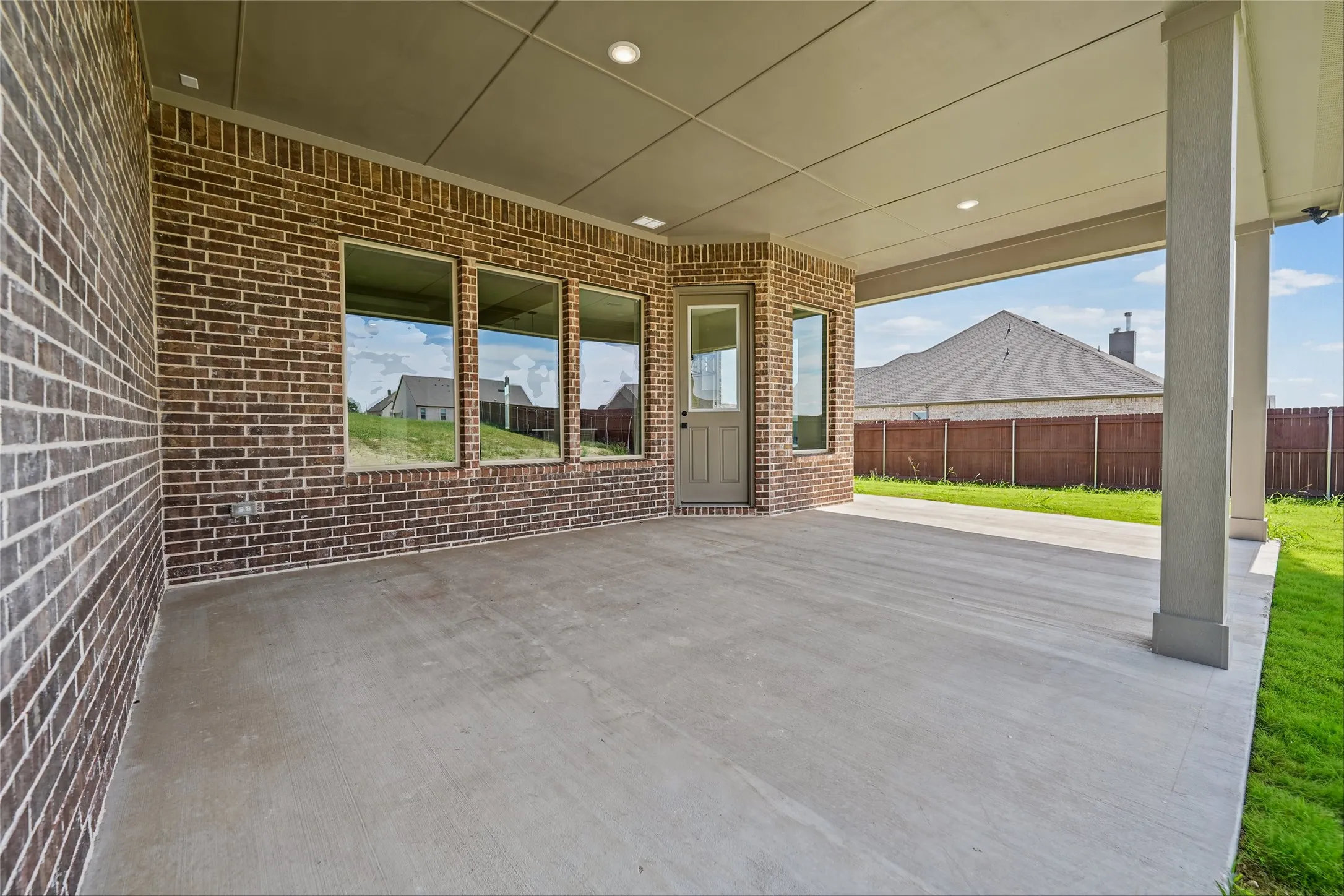 Covered patio with brick exterior, concrete flooring, recessed lighting, and a paneled door