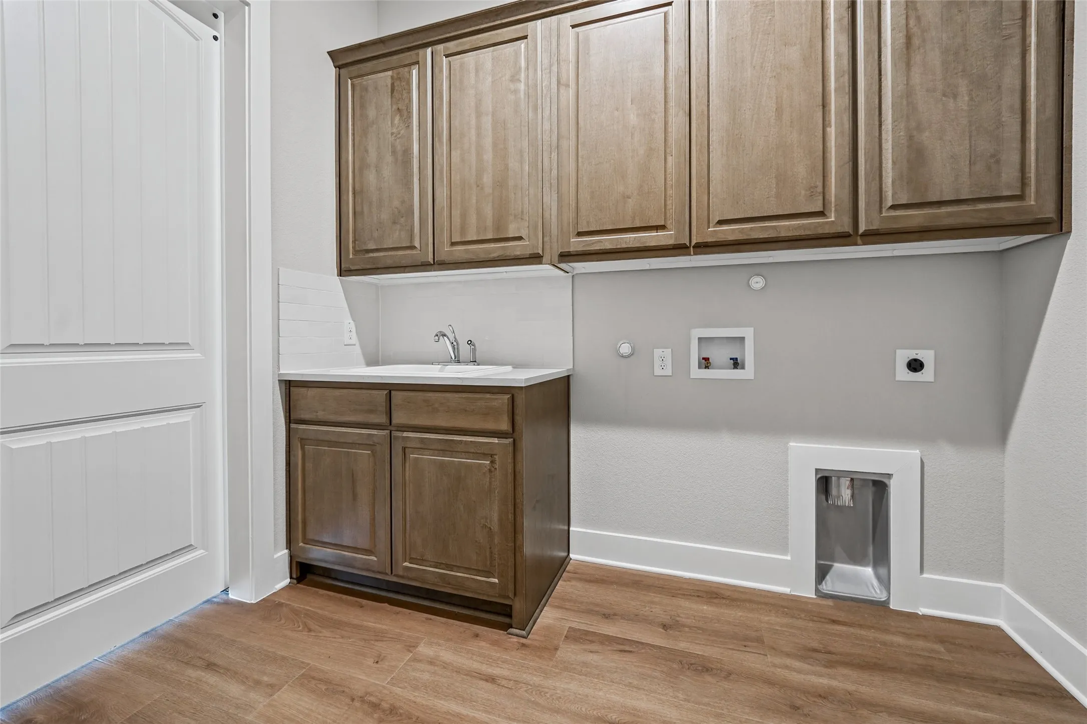 Wood-finish flooring, built-in cabinetry, sink with faucet, white subway tile backsplash, and a white paneled door