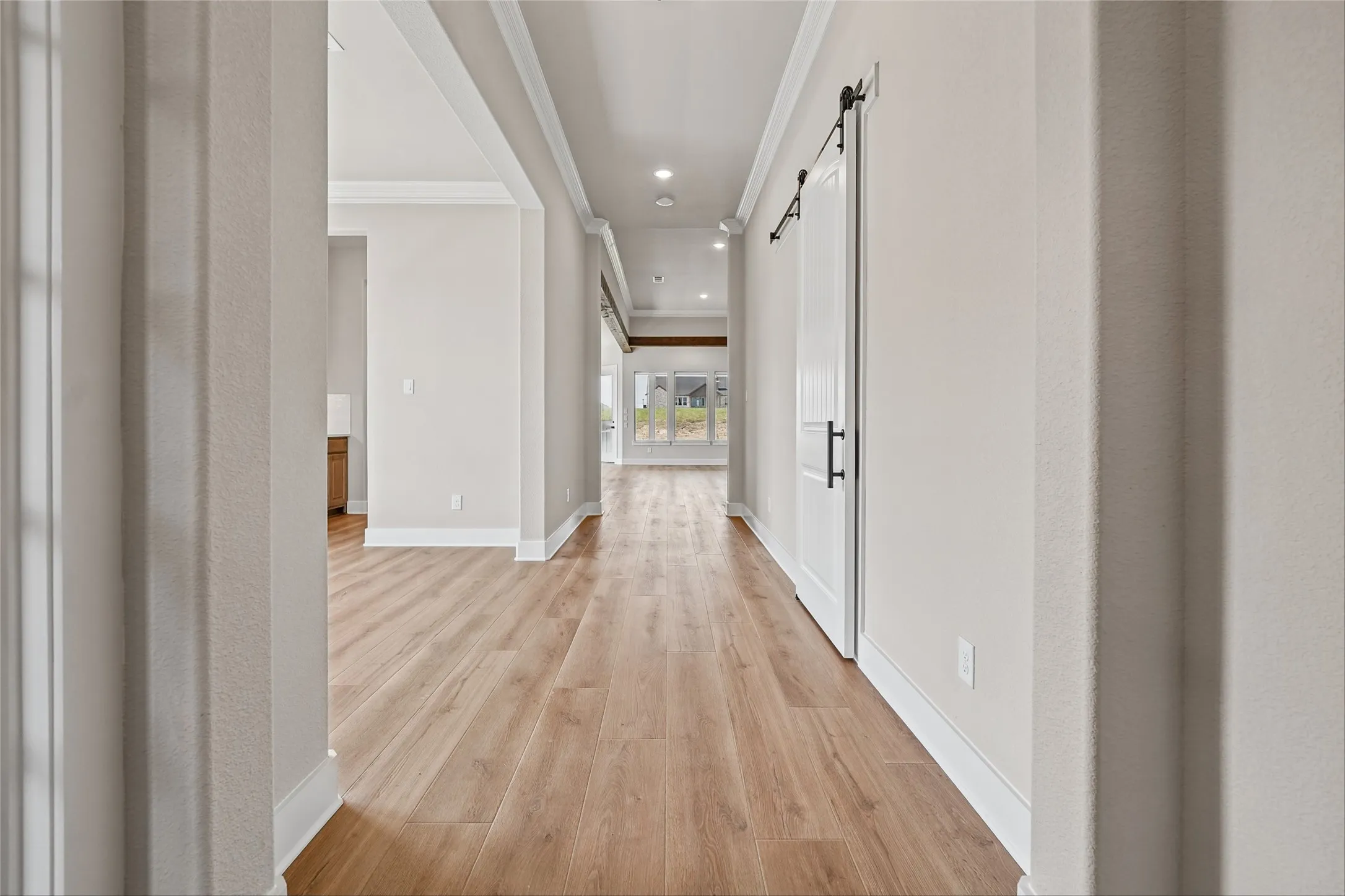Hallway with wood-finish flooring, recessed lighting, white crown molding, and a barn door