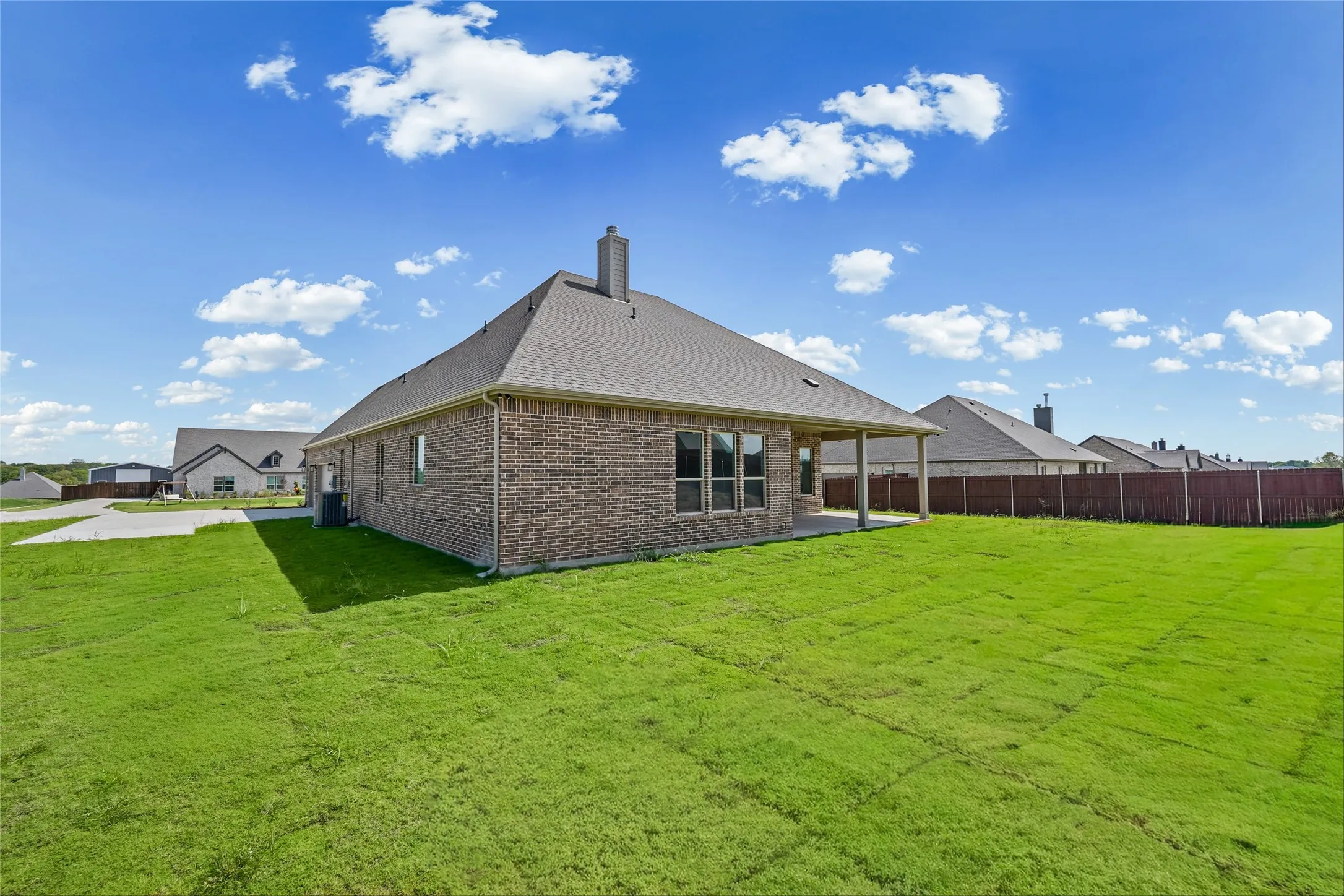 Expansive green lawn, brick exterior, covered patio, multiple windows, and a shingled roof