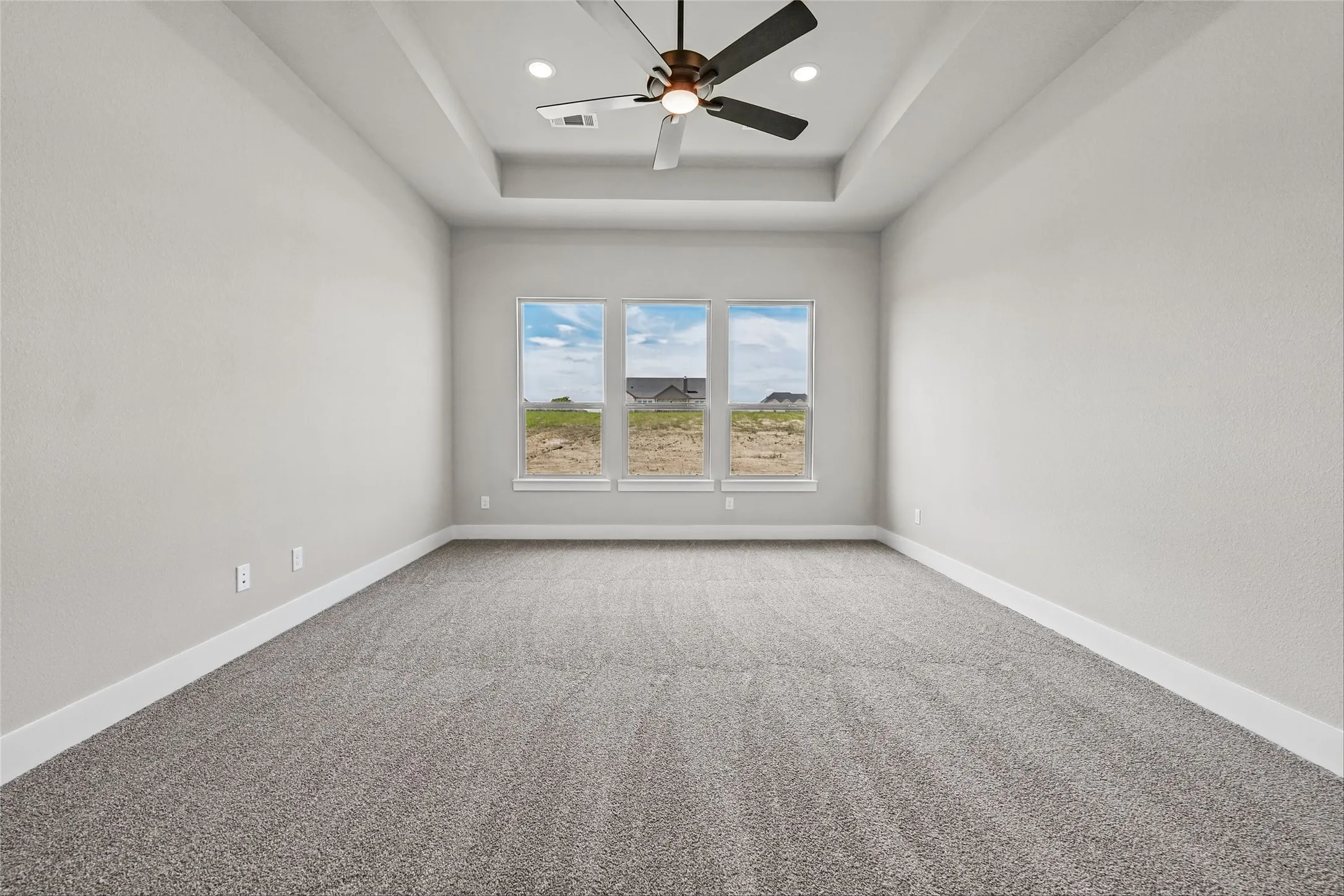 Tray ceiling with recessed lighting and a ceiling fan, light gray wall finishes, gray carpet flooring, and three rectangular windows