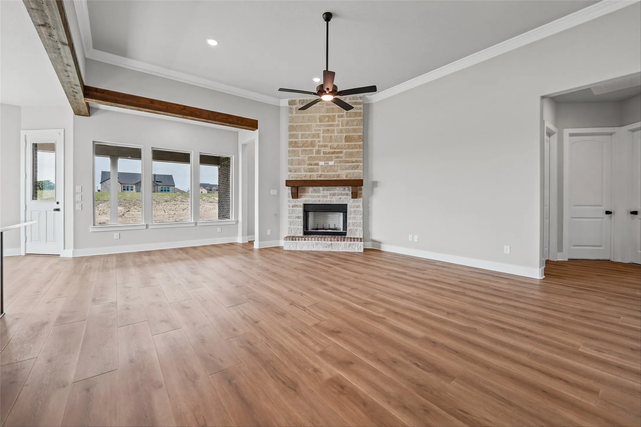 Wood-finish flooring throughout, vaulted ceiling with exposed wood beams, stone fireplace with a wood mantle, and multiple transom windows