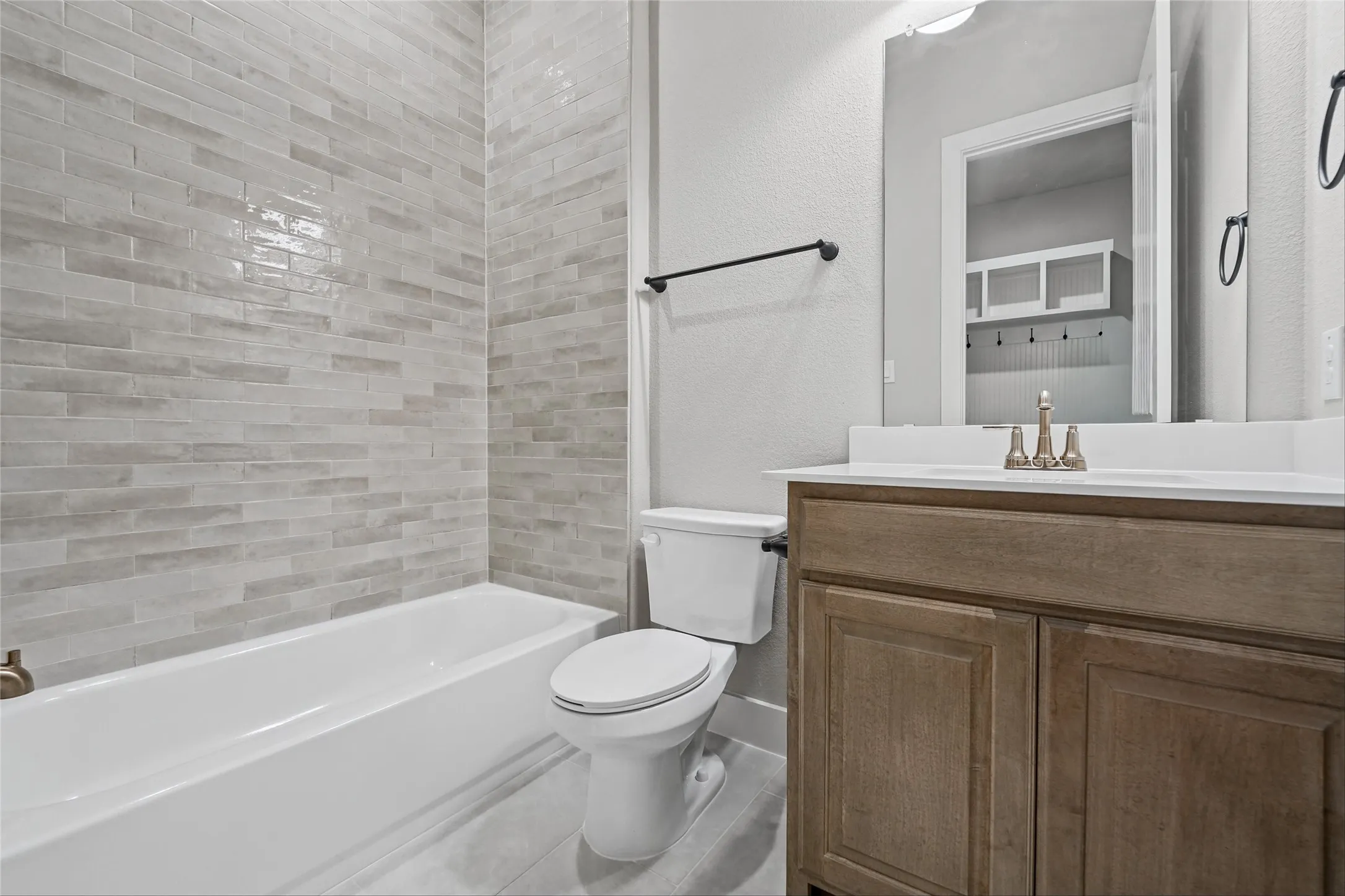 Bathtub with light-toned subway tile surround, wood-finish vanity with countertop, and integrated sink