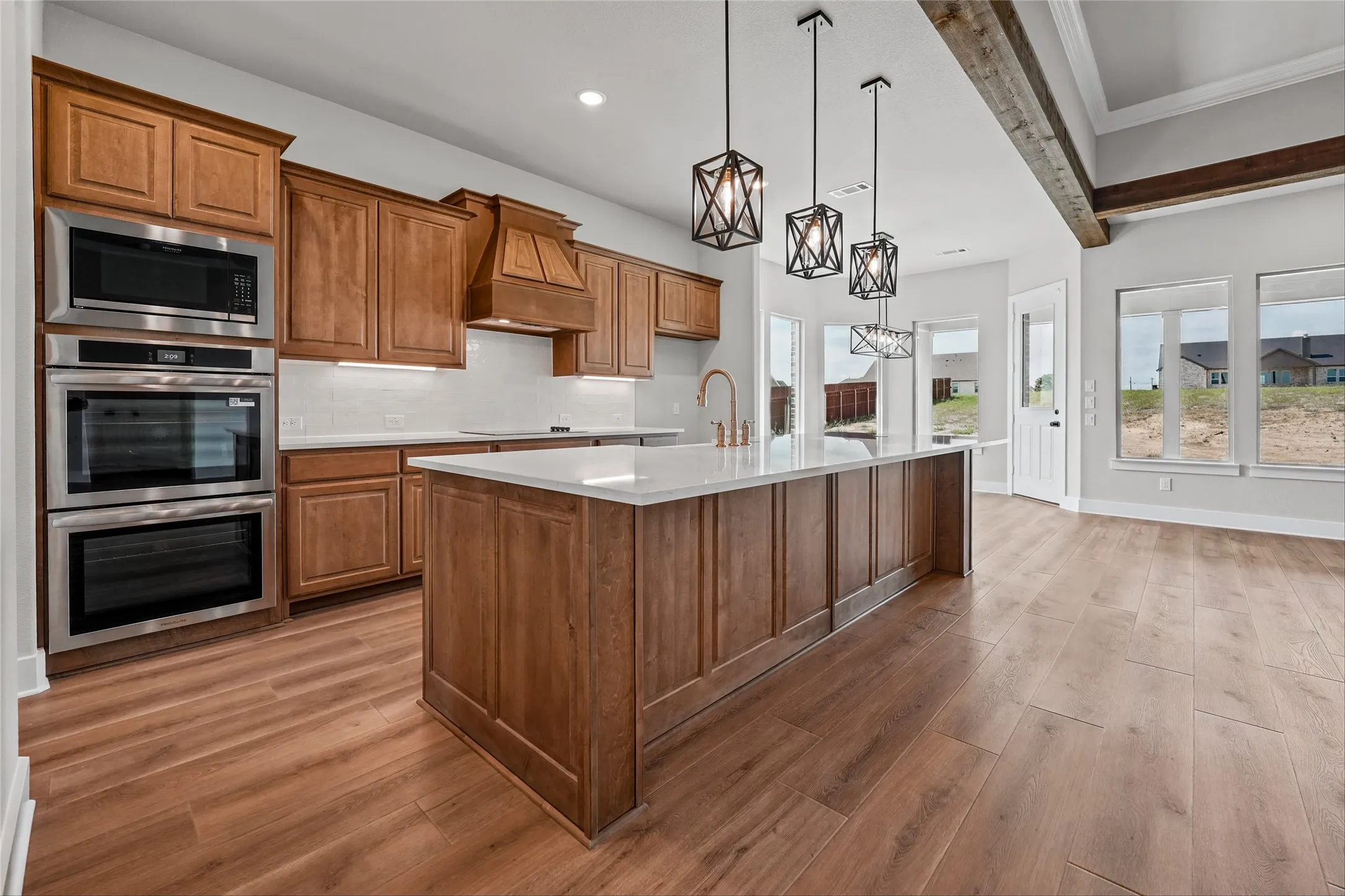 Gourmet kitchen with wood-finish flooring, custom wood cabinetry, stainless steel double oven, and a large central island with pendant lighting
