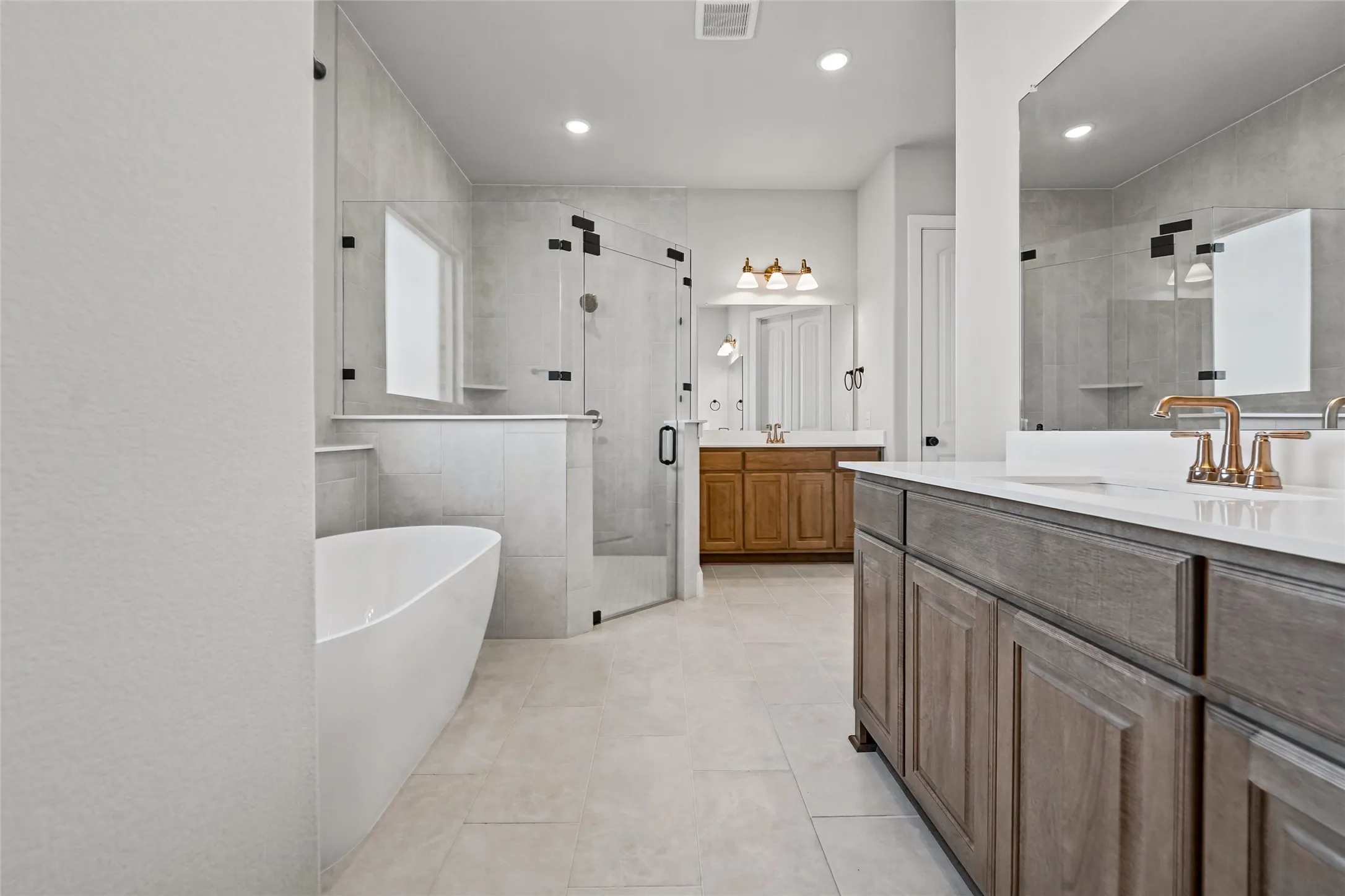 Freestanding soaking tub, glass-enclosed shower, dual vanities with integrated sinks, and tile flooring