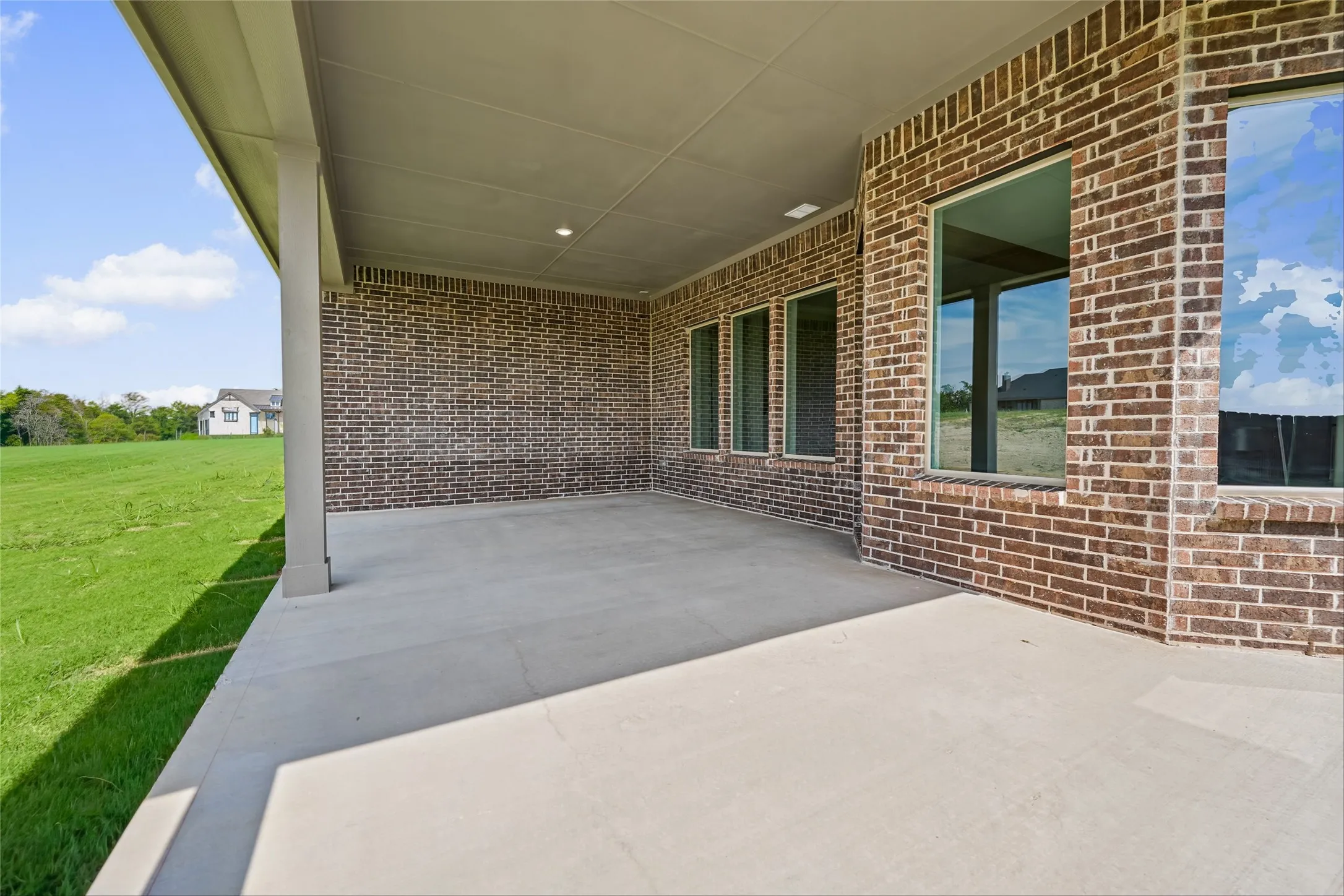 Expansive covered concrete patio featuring brick exterior, recessed lighting, and large windows