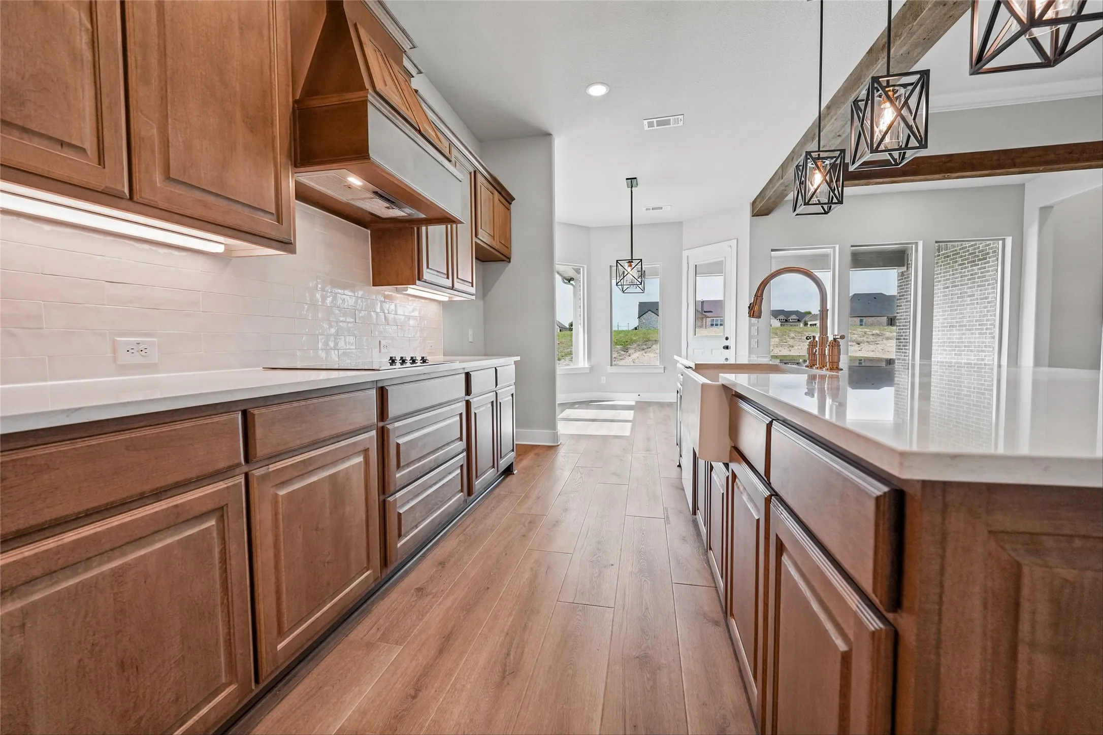 Wood-finish flooring, island with farmhouse sink and gooseneck faucet, light-colored countertops, tiled backsplash, and recessed lighting