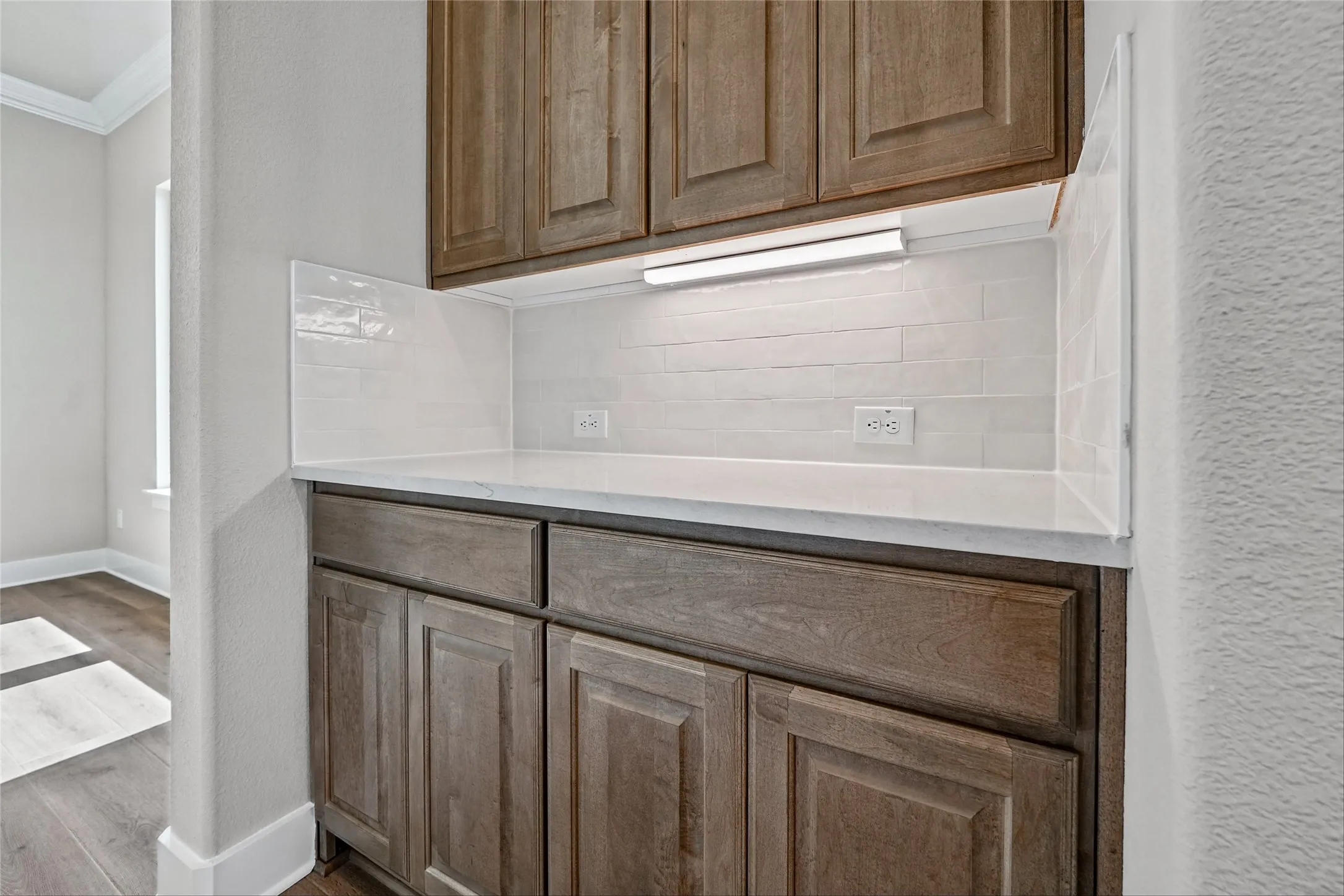 Built-in cabinetry with wood-finish doors and drawers, white countertop, white tile backsplash, and task lighting