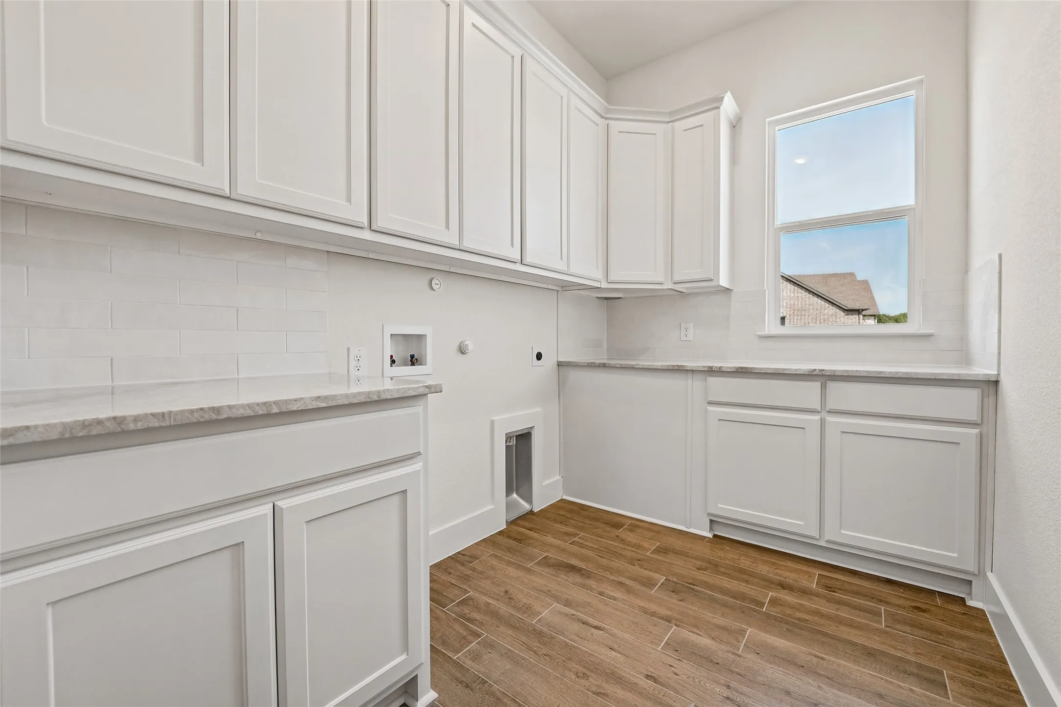 White shaker-style cabinetry, wood-finish tile flooring, white subway tile backsplash, and light-toned countertops