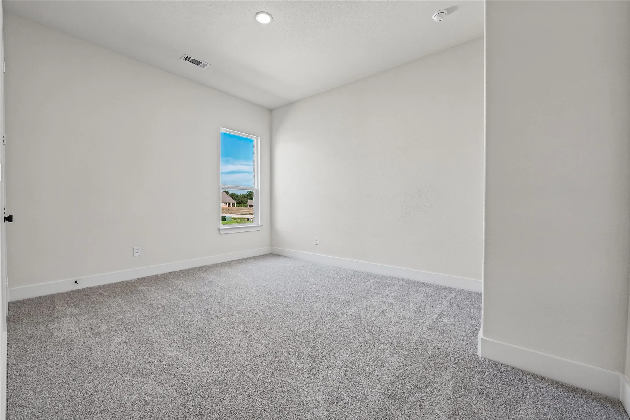 Neutral paint palette, recessed ceiling lighting, light gray carpet, window with exterior scenery, and white trim
