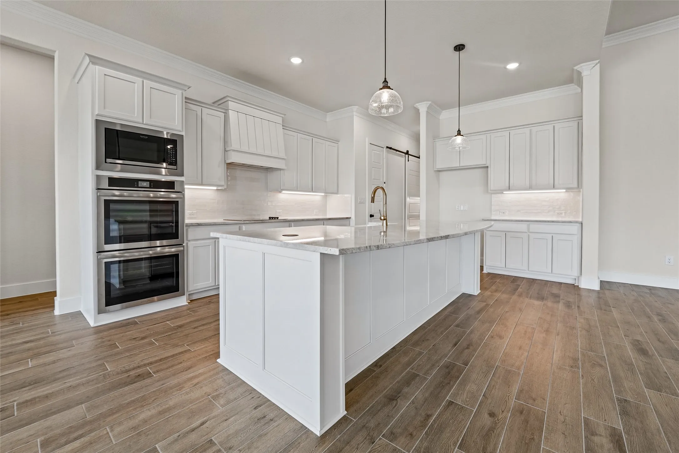 Kitchen featuring a large center island with a stone countertop, built-in double ovens, white shaker cabinetry, pendant lighting, and wood-finish flooring
