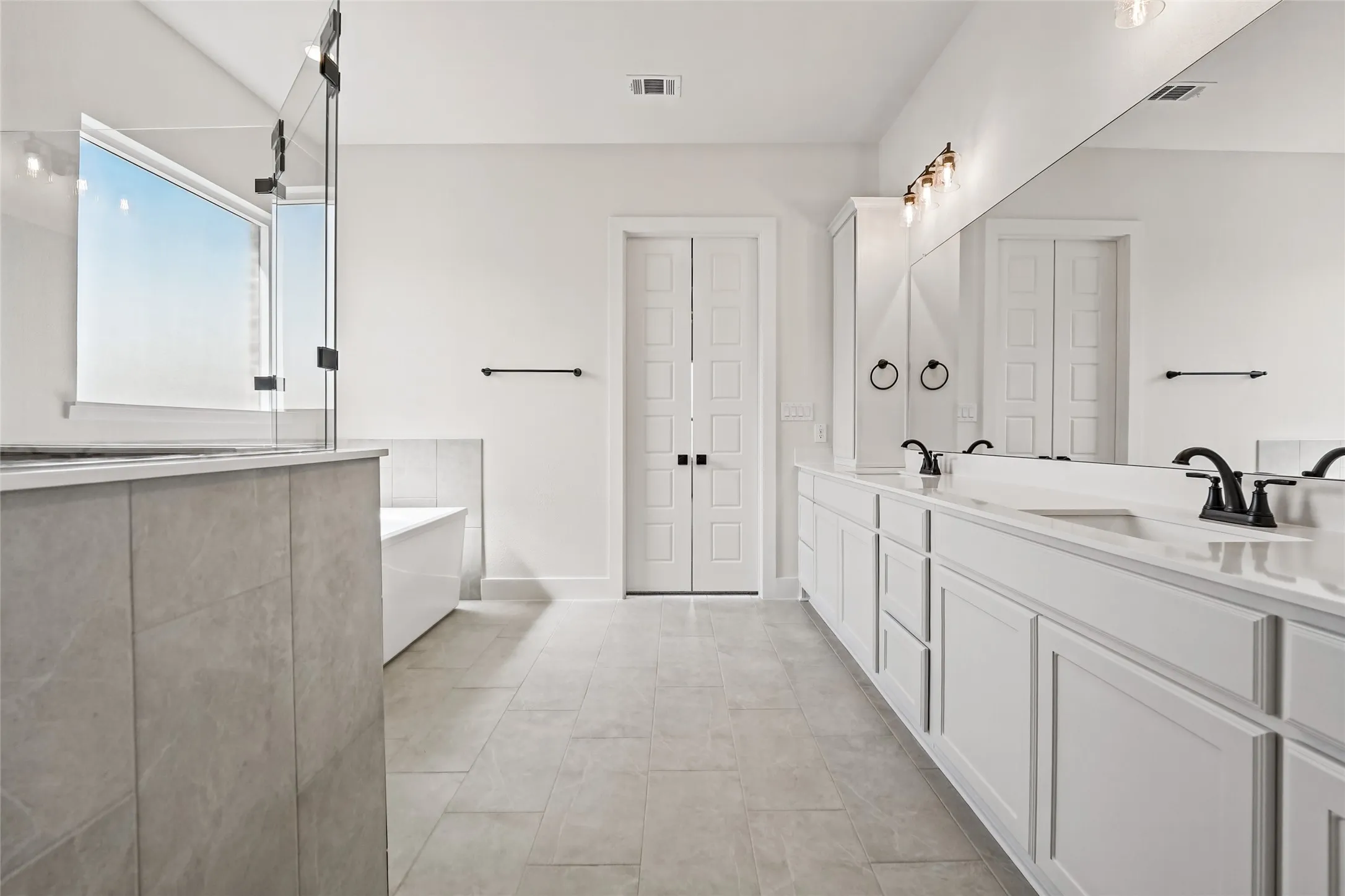 Dual vanity with white cabinetry and integrated sinks, matte black plumbing fixtures, large frameless mirror, and tiled flooring