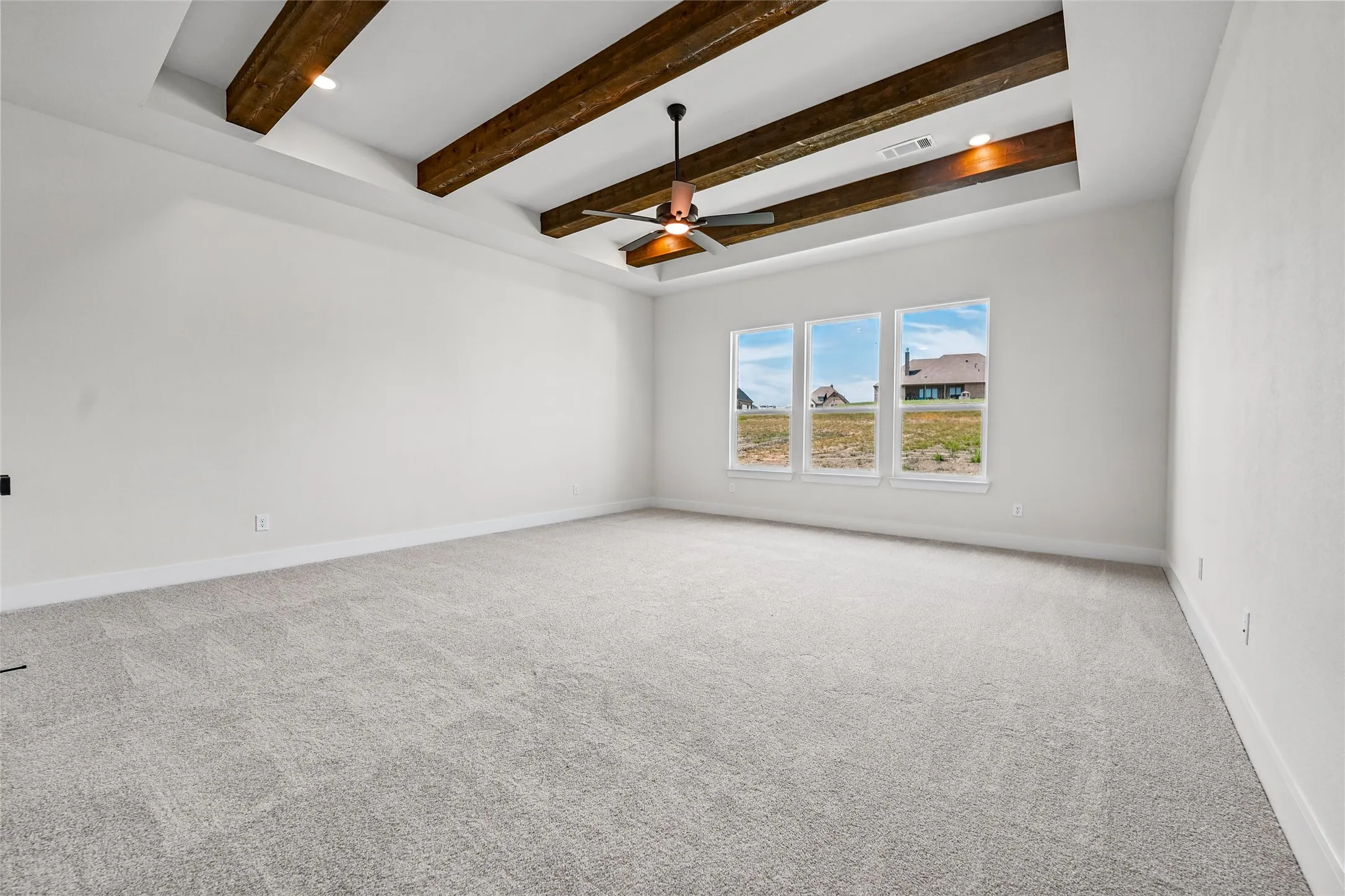 Tray ceiling with exposed wood beams, ceiling fan, recessed lighting, and three large windows