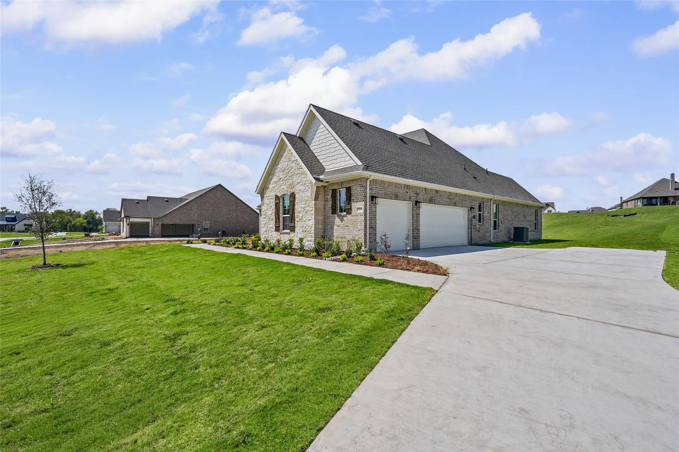Cream brick exterior with white trim, dark shingle roof, and a two-car garage