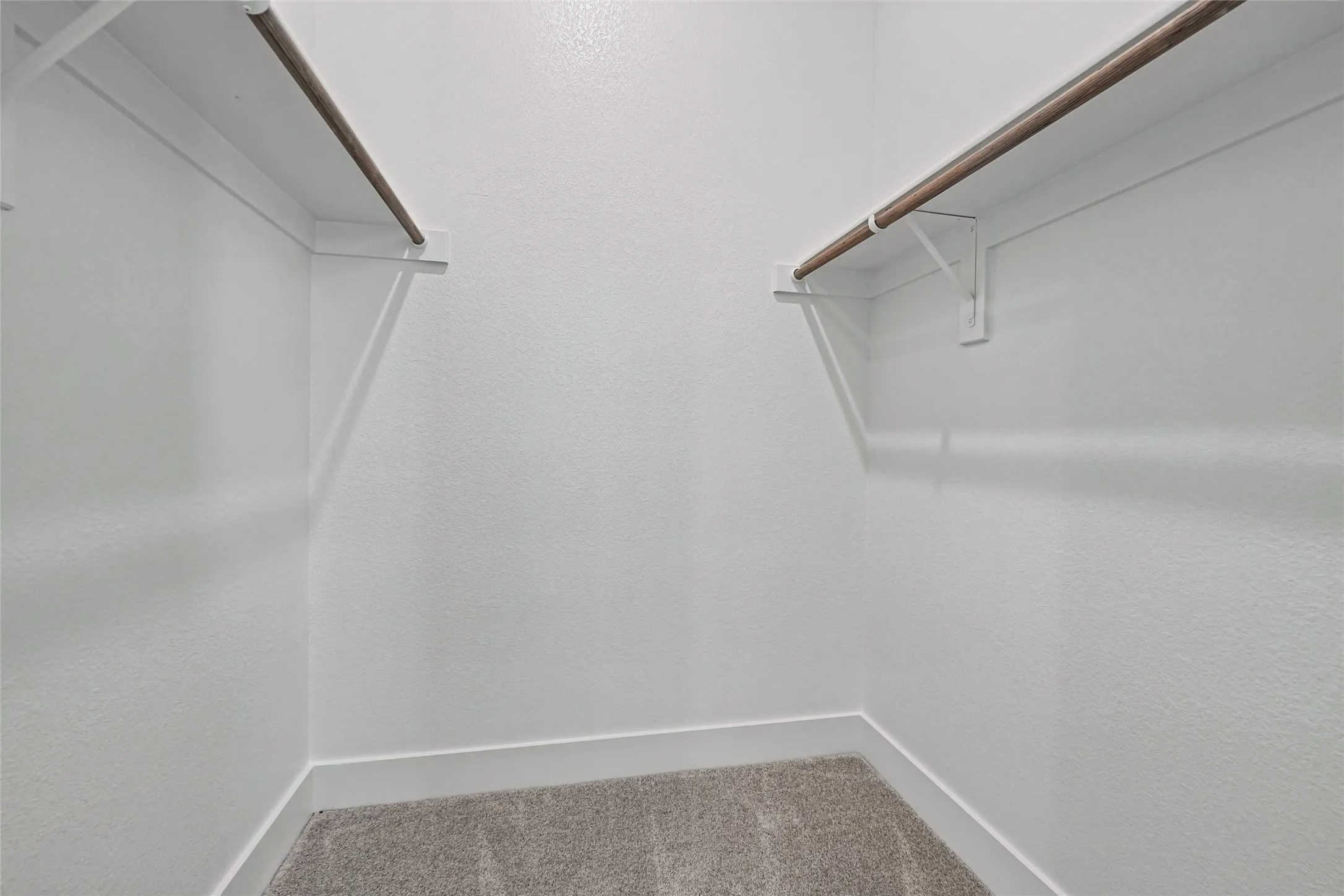 Carpeted closet with dual wood-finish hanging rods and white shelving