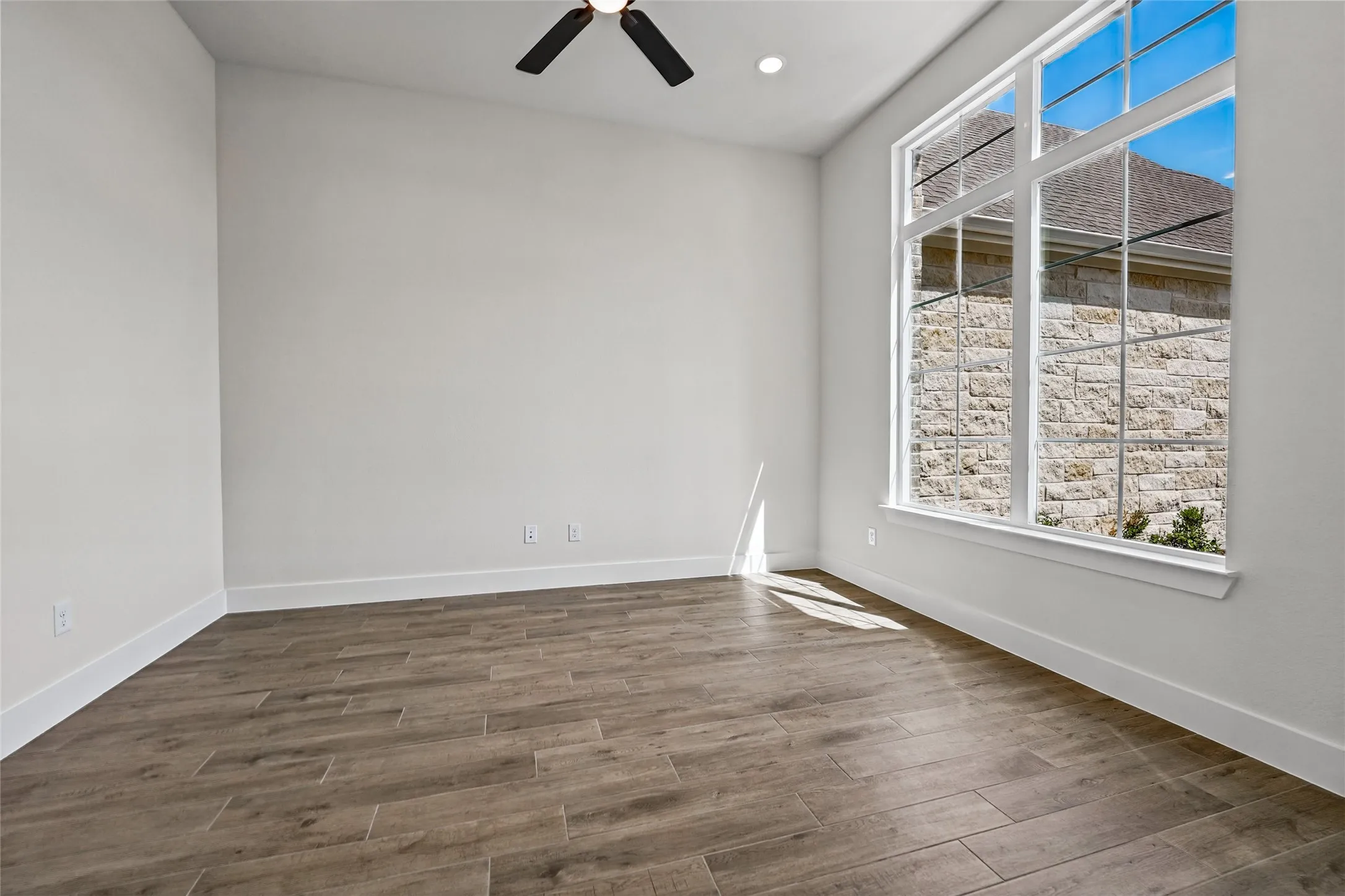 Spacious room with wood-finish flooring, a large multi-pane window, recessed lighting, and a ceiling fan