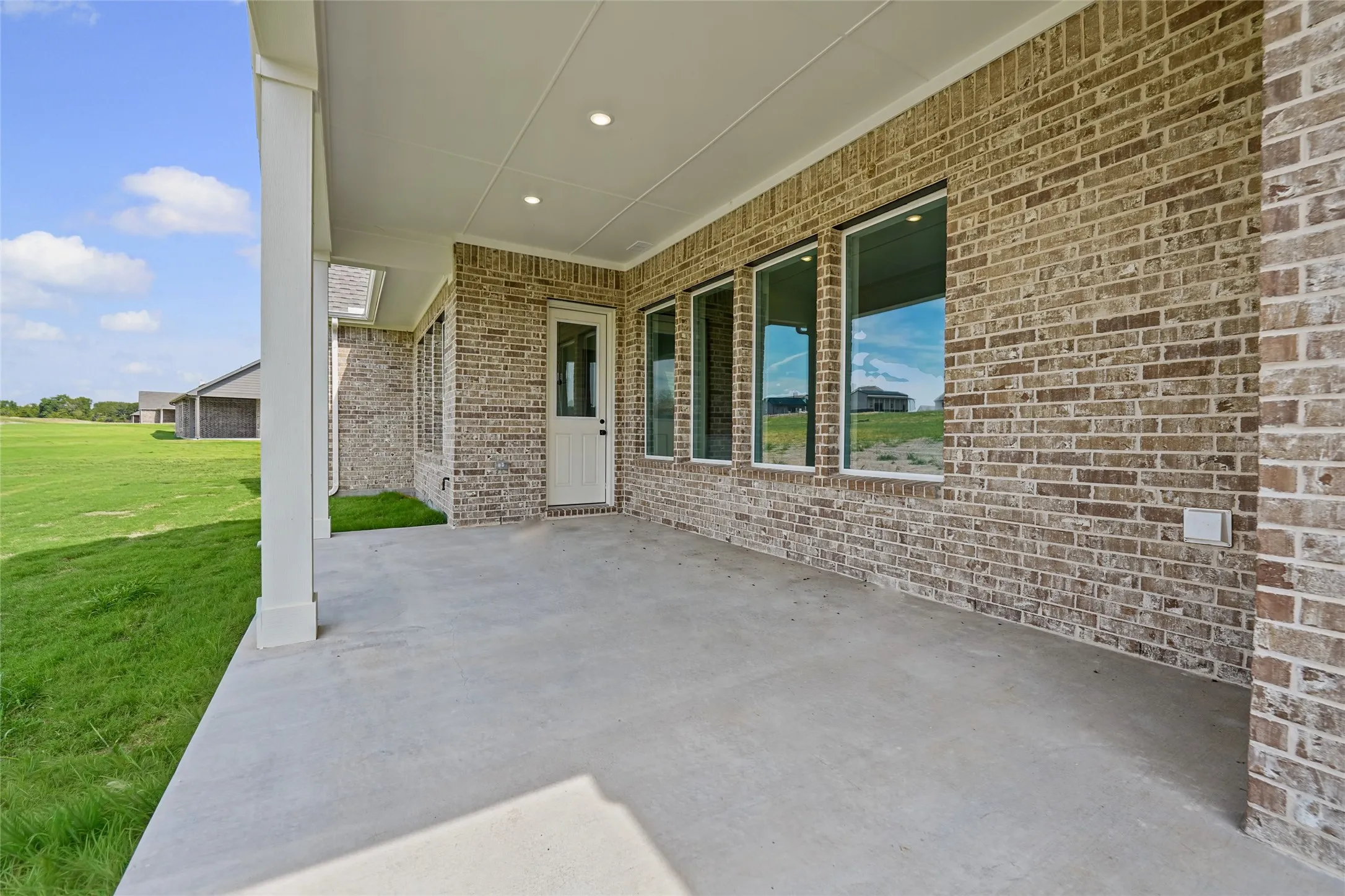 Covered concrete patio with recessed lighting, brick exterior, and multiple large windows