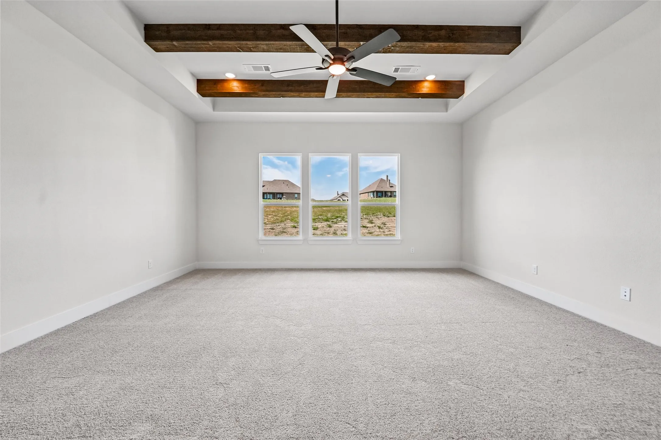 Recessed tray ceiling with wood beams, ceiling fan, triple windows, and neutral carpet flooring