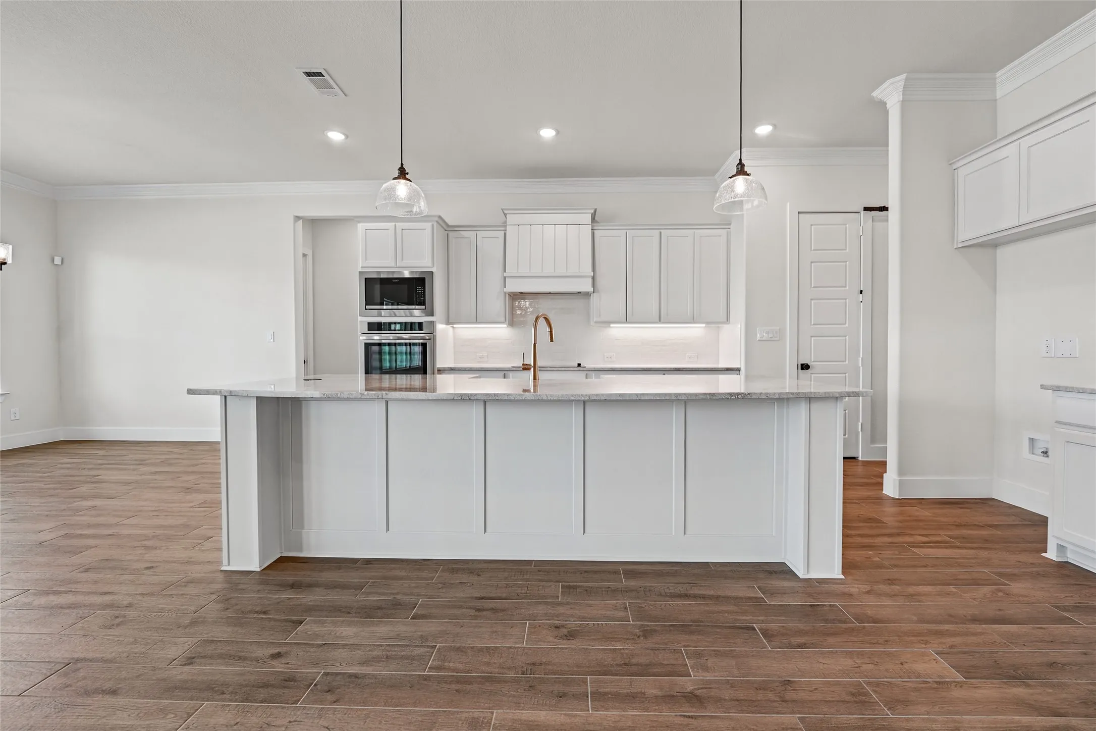Kitchen featuring a spacious island with a light-toned countertop, white cabinetry with gold-toned hardware, and wood-finish flooring