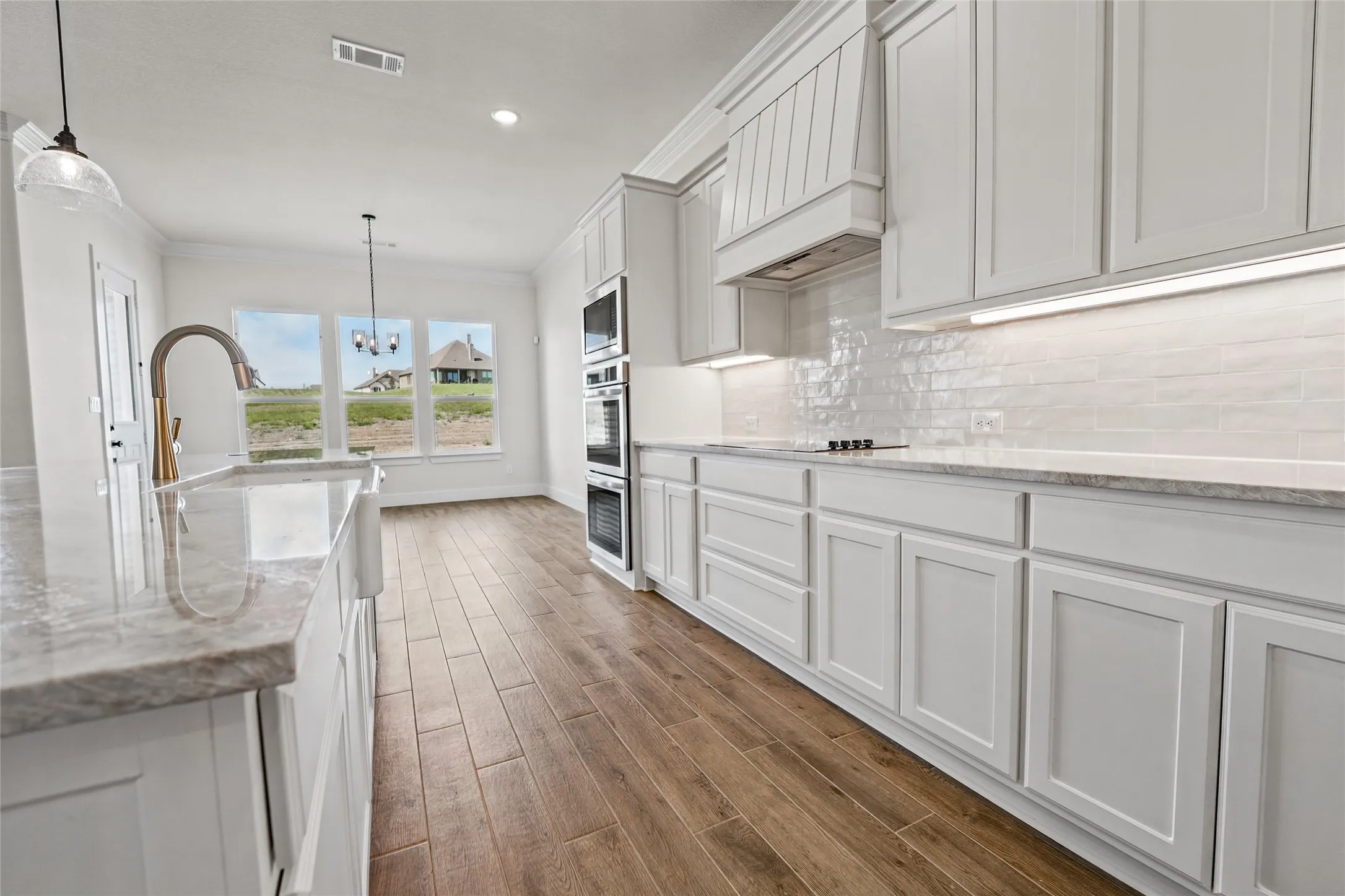 Wood-finish flooring, white shaker-style cabinetry, double wall ovens, a farmhouse sink, and a tiled backsplash