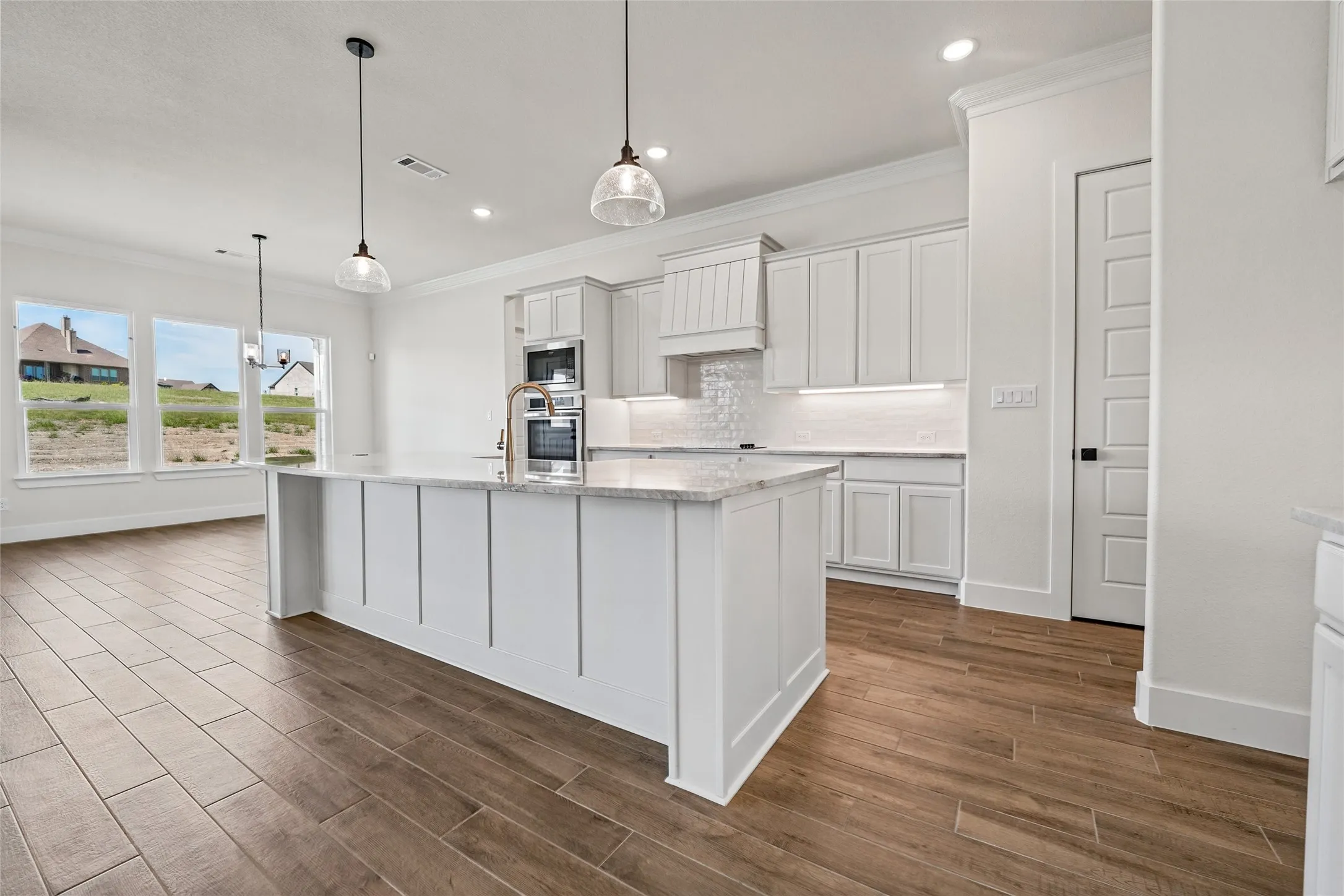 Open concept kitchen with wood-finish flooring, white cabinetry, a large center island with a stone countertop, and stainless steel built-in appliances