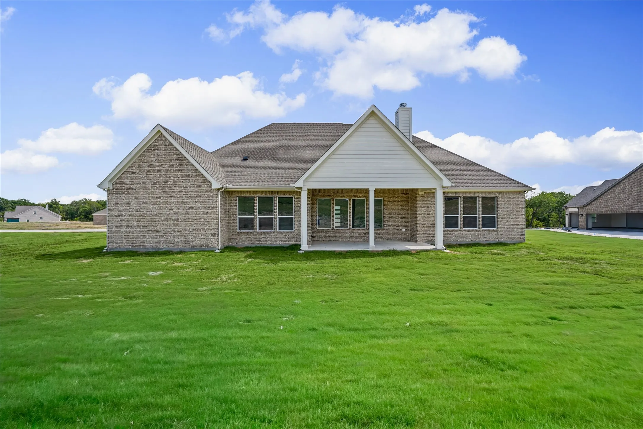 Expansive rear lawn, brick exterior, covered patio, multiple windows, and a shingled roof