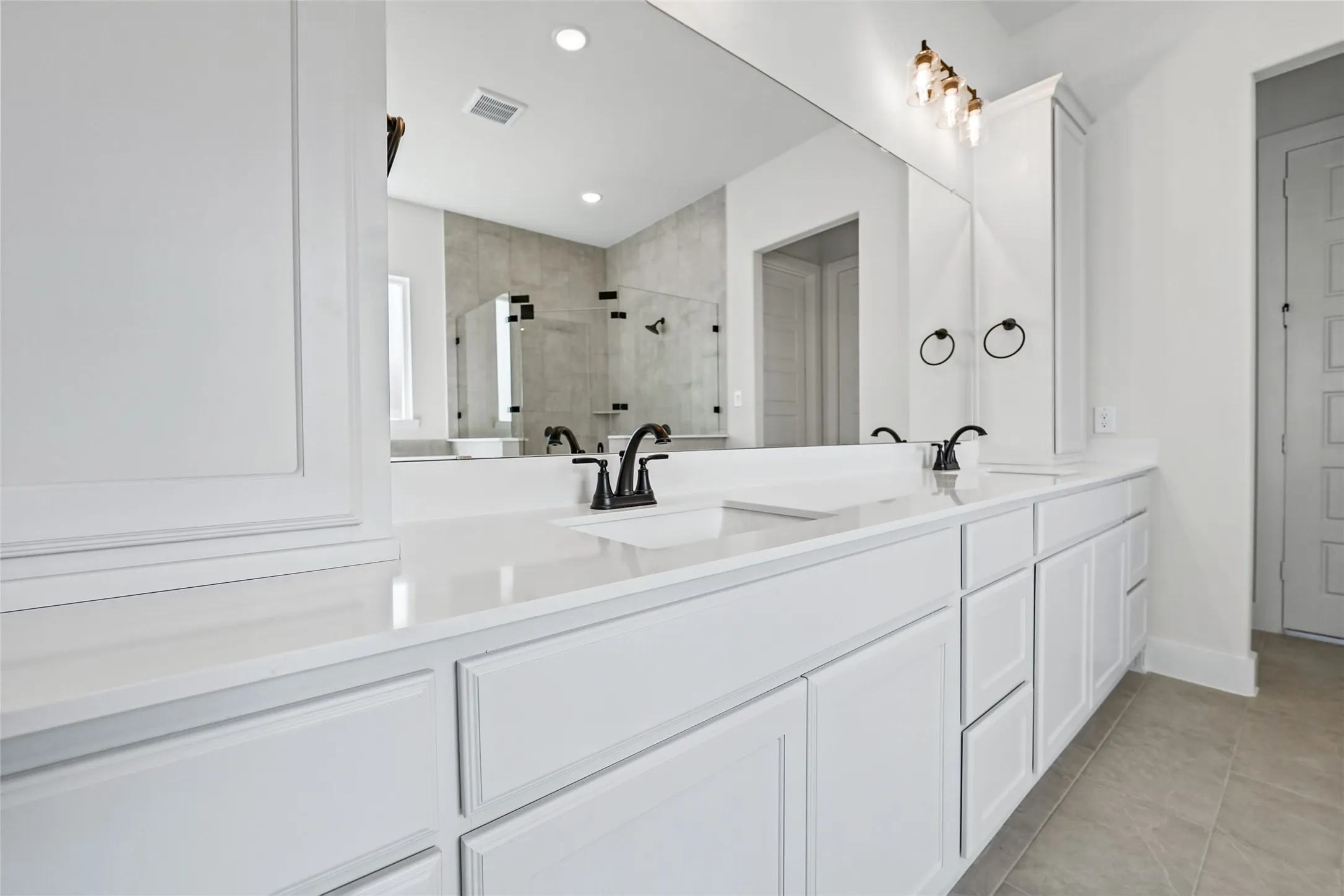 Dual vanity with white cabinetry and integrated sinks, quartz-finish countertops, matte black hardware, and a framed mirror