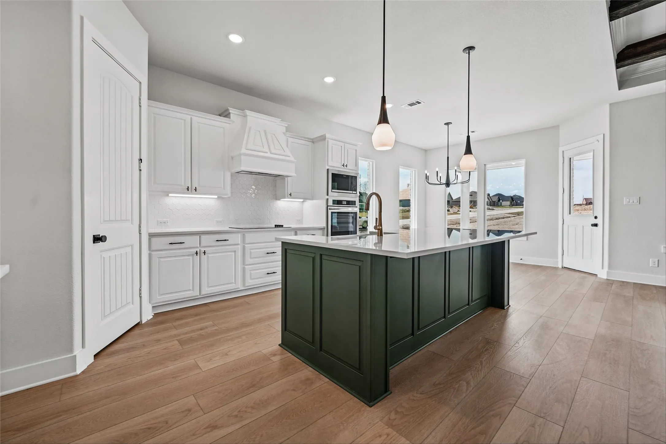 Spacious kitchen featuring a dark green center island with a white countertop, white cabinetry with dark hardware, integrated stainless steel appliances, and wood-finish flooring
