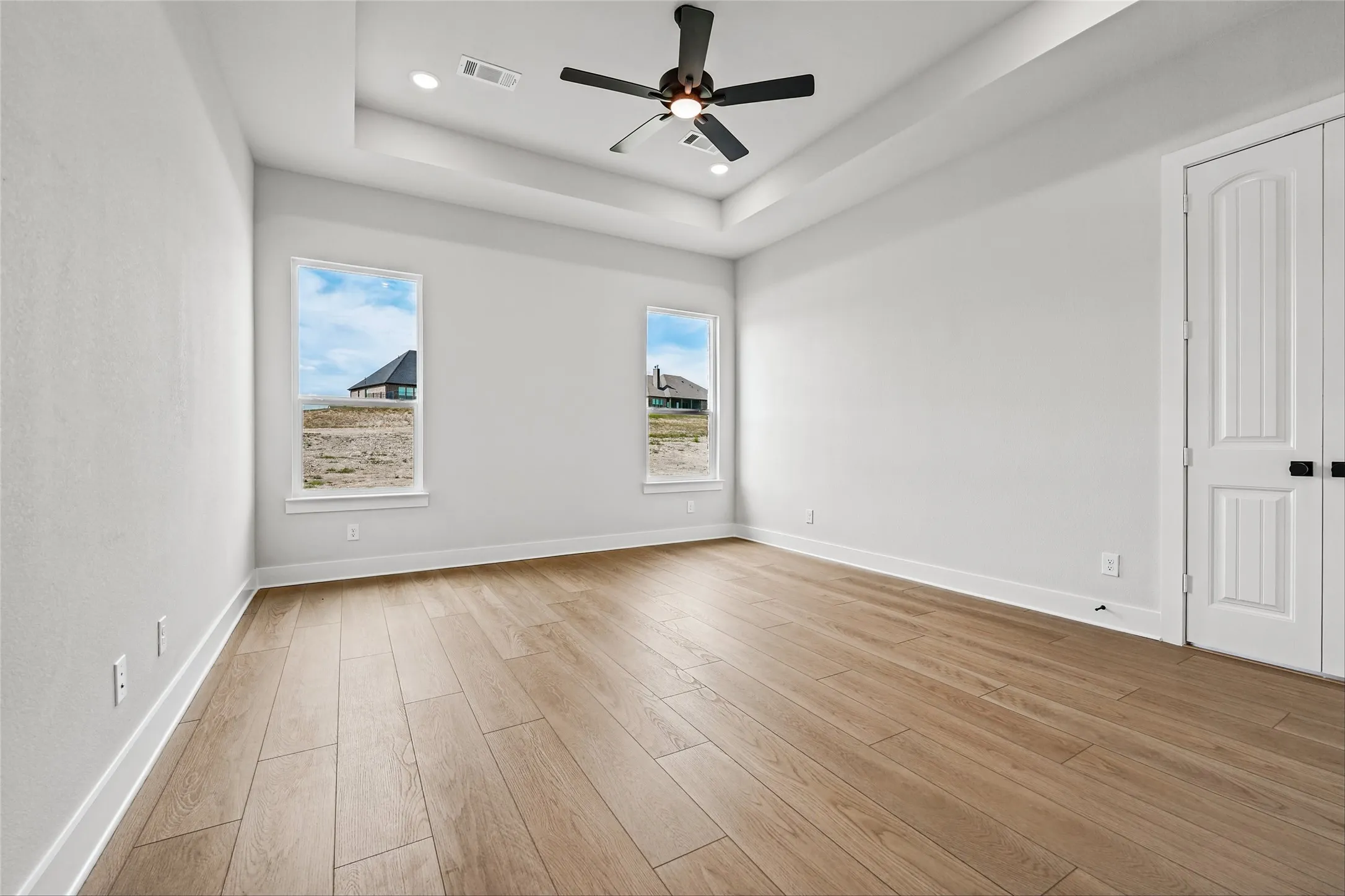 Tray ceiling with recessed lighting, wood-finish flooring, and white paneled doors