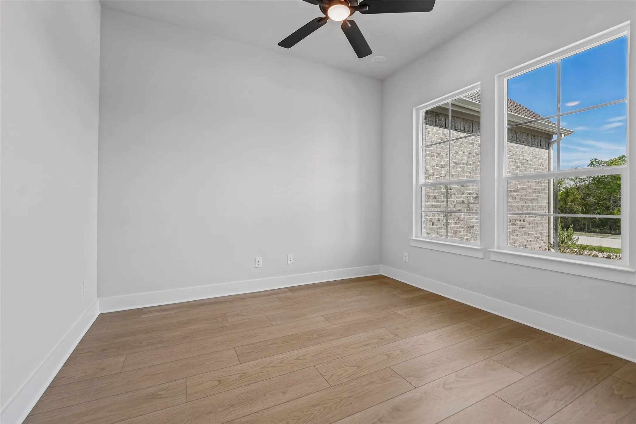 Bright room featuring wood-finish flooring, two large windows with white trim, and a ceiling fan