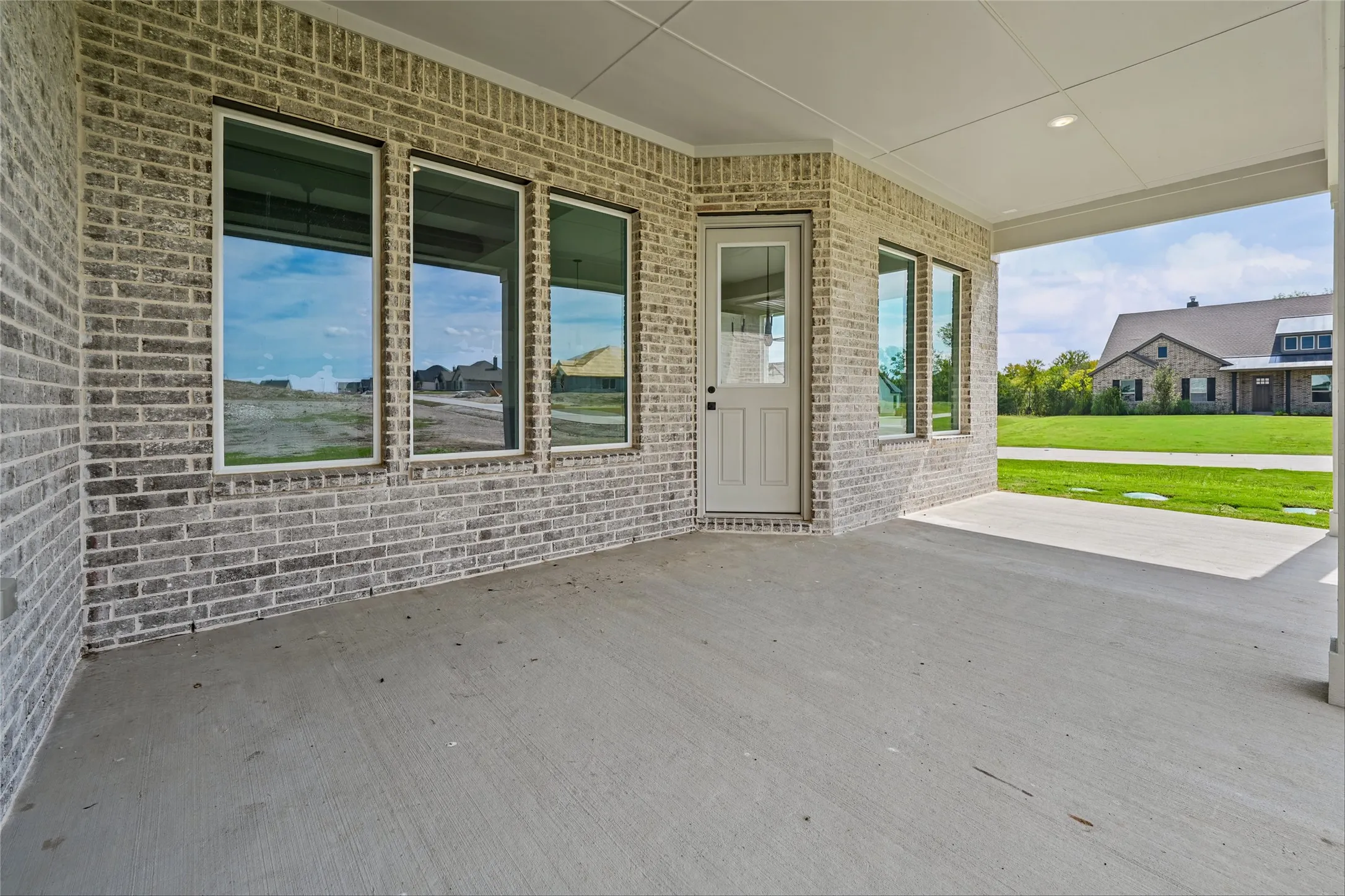 Covered concrete patio with recessed lighting, brick exterior, and a glass-paneled door